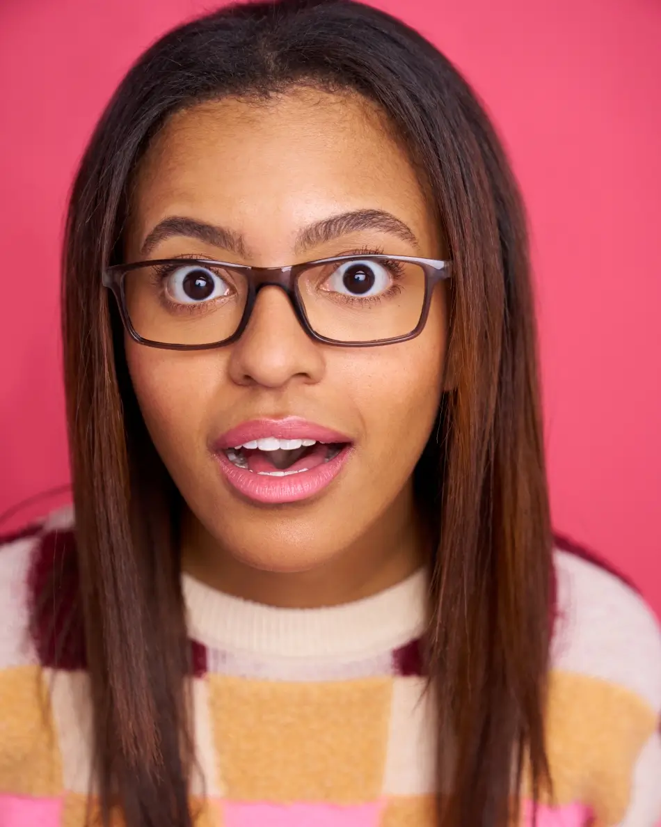 Atlanta teen actor headshot — teen girl with straight brown hair and glasses, wide-eyed expressive look in colorful sweater against pink background, theatrical expressive teen character look.