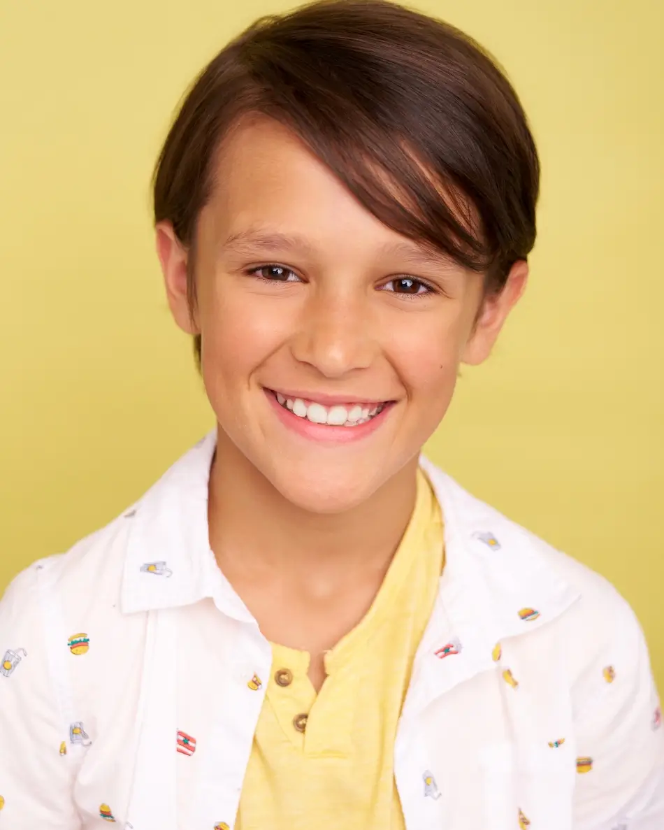 Atlanta kids actor headshot — young boy with brown hair and bright smile in yellow shirt and patterned white button-up against yellow background, cheerful bright commercial kids look.