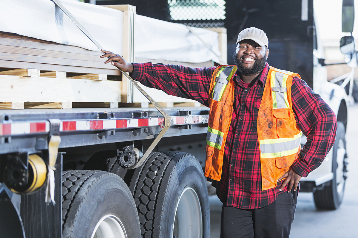 Delivery driver standing next to a truck loaded with construction materials, ready for on-time delivery to a construction site.