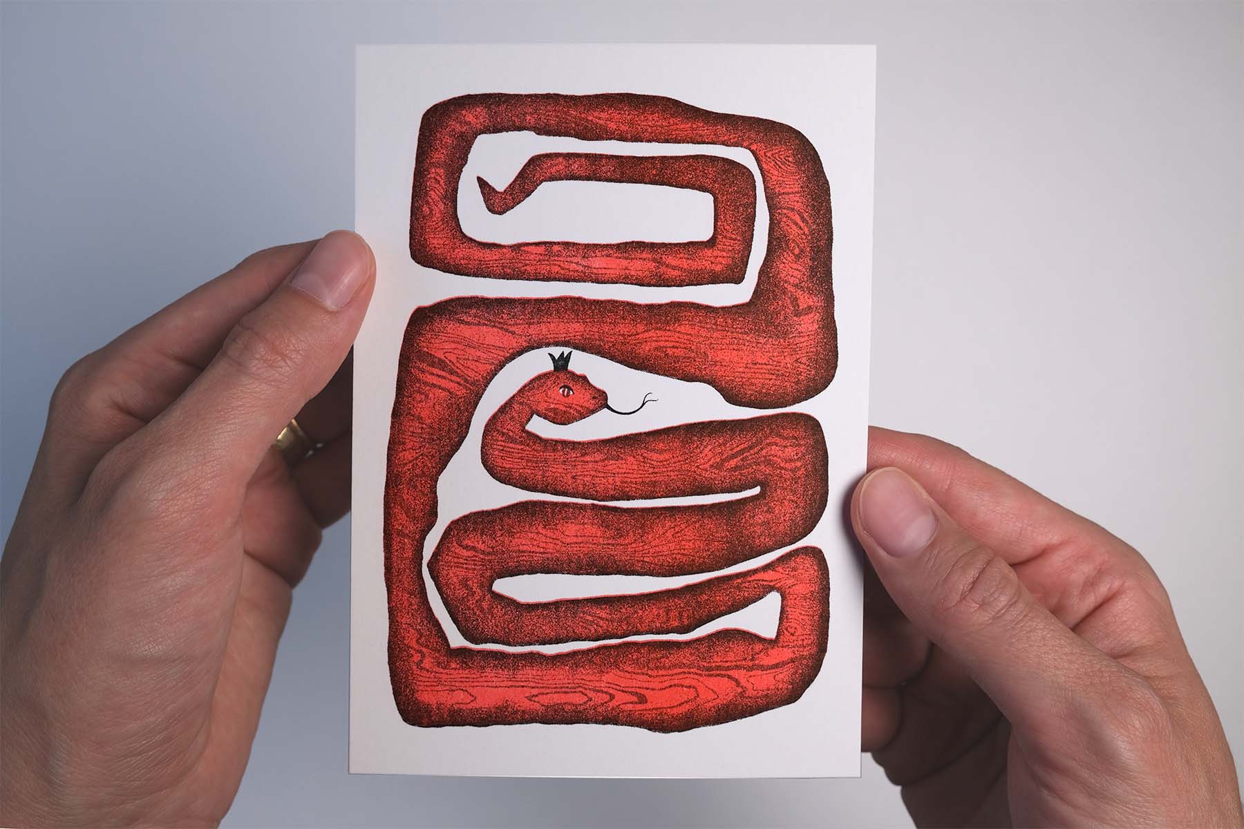 Hand holding an A6 risograph print of the snake