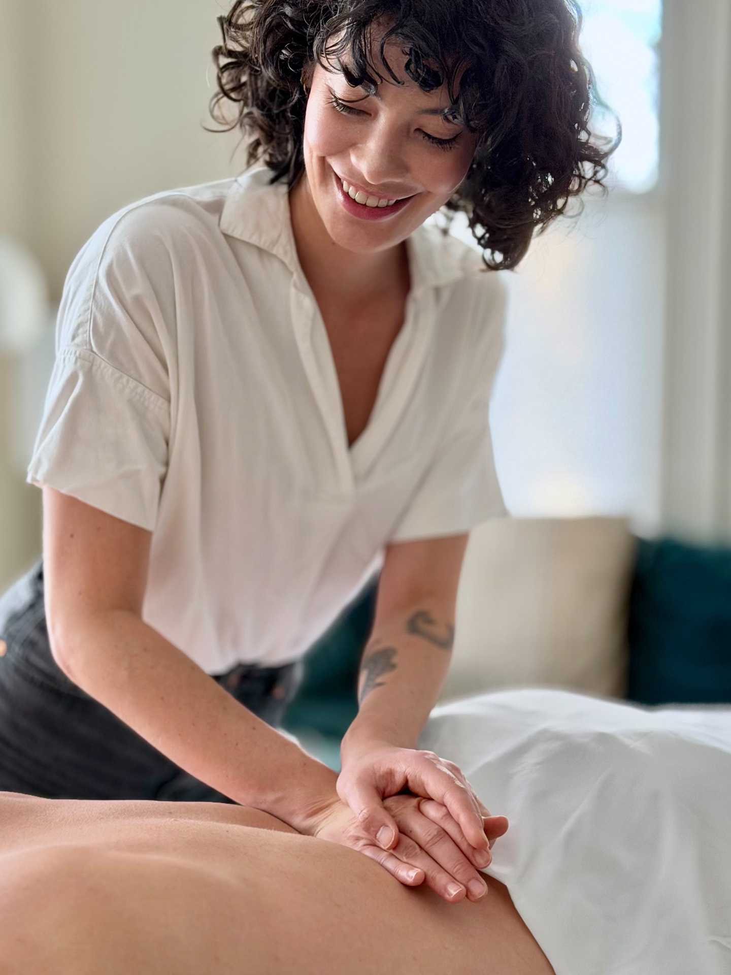 Anna Kimura smiling warmly while using both hands to apply targeted manual therapy to a patient's lower back.