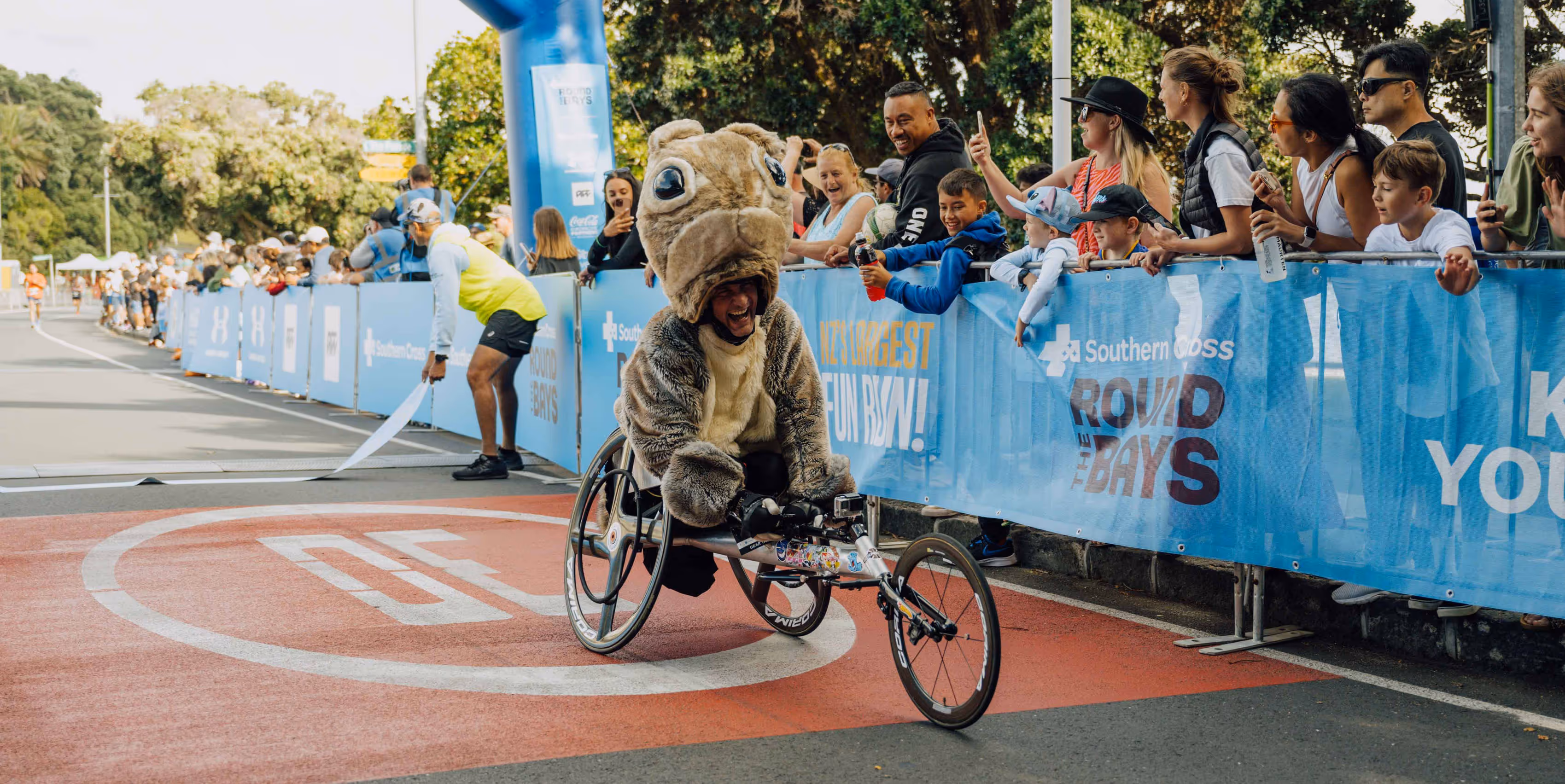 A man in fancy dress racing in a wheelchair crosses the finish line at a race