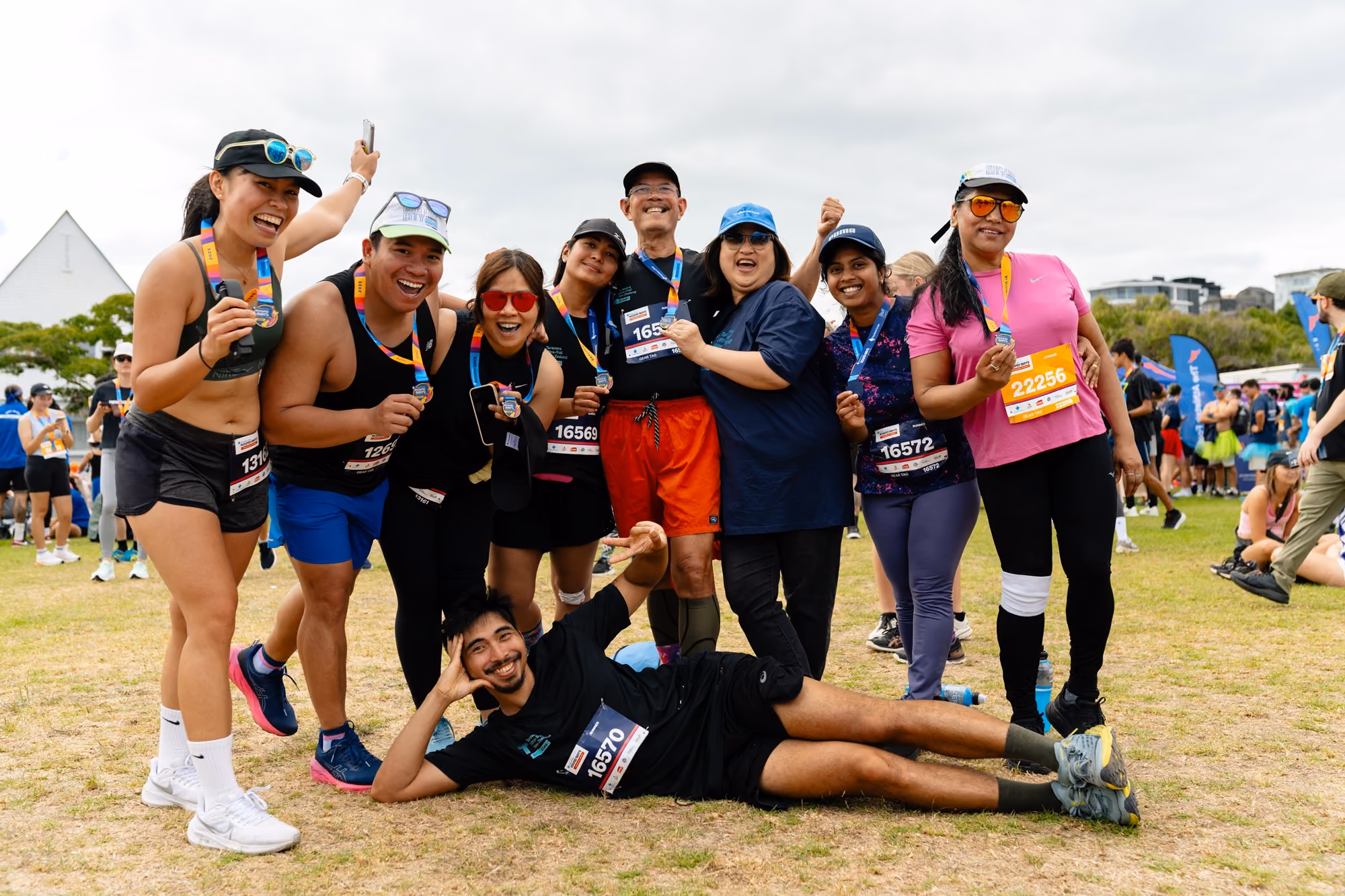 Group of runners smiling and posing with medals outdoors on grass after race event.