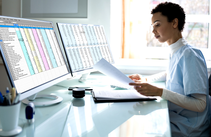 Ethnic businesswoman performing coding and billing operations on double monitors.