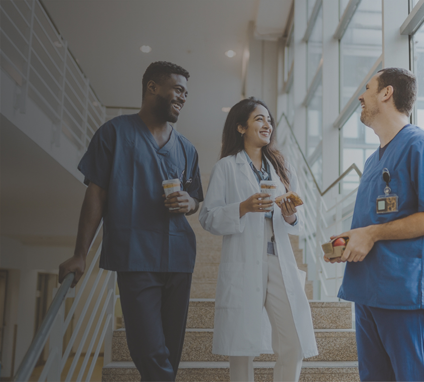 Group of three doctor's talking on the stairway of hospital with coffee and lunch items in hand.