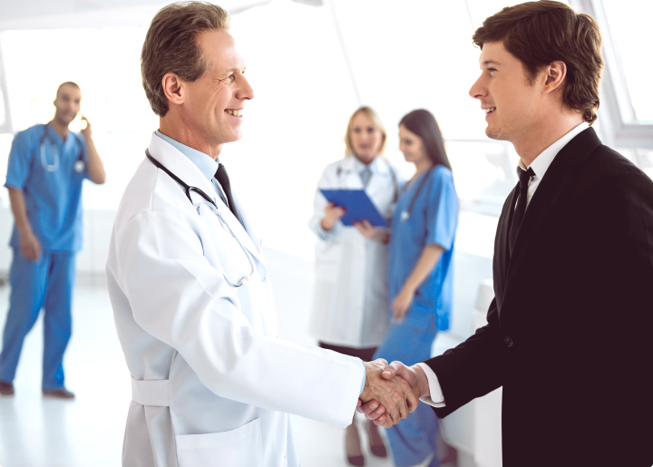 Older male physician shaking hands with a younger businessman.