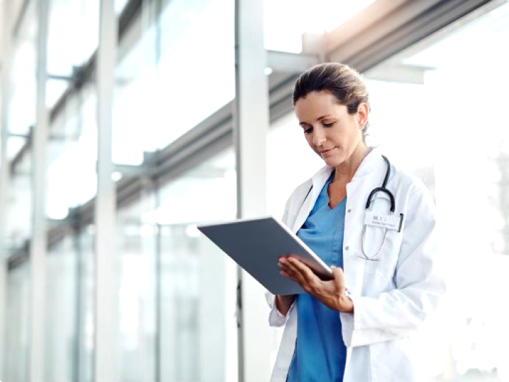 Female physician standing in front of a hospital window and working on a digital tablet.