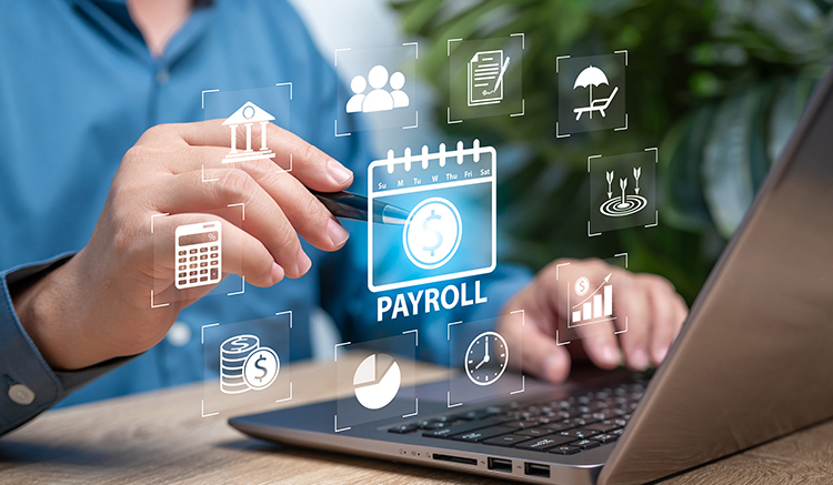 Composited image of hands and pen pointing to a hovering payroll dashboard floating above a laptop.