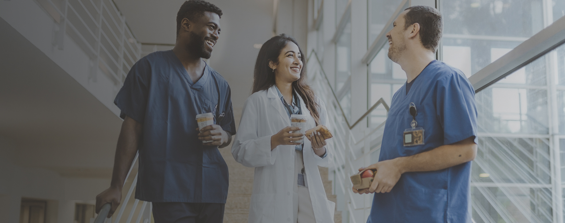 Group of three doctor's talking on the stairway of hospital with coffee and lunch items in hand.