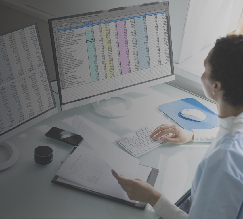 Ethnic businesswoman performing coding and billing operations on double monitors.