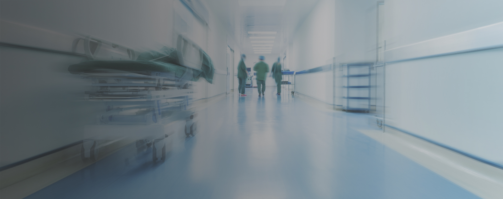 A blurred image of doctors walking down an emergency room hallway.