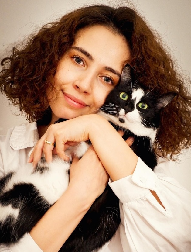 Jeune femme aux cheveux bouclés tenant et câlinant un chat noir et blanc aux yeux verts.