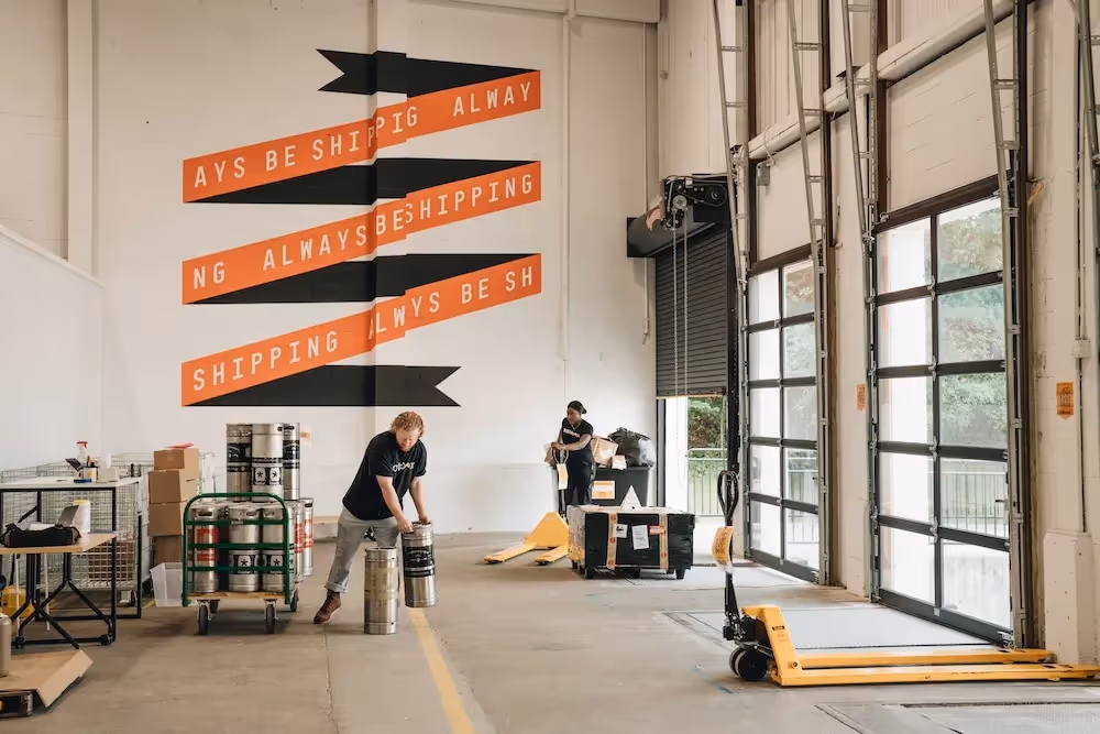 A man and a woman in a warehouse moving containers and boxes.