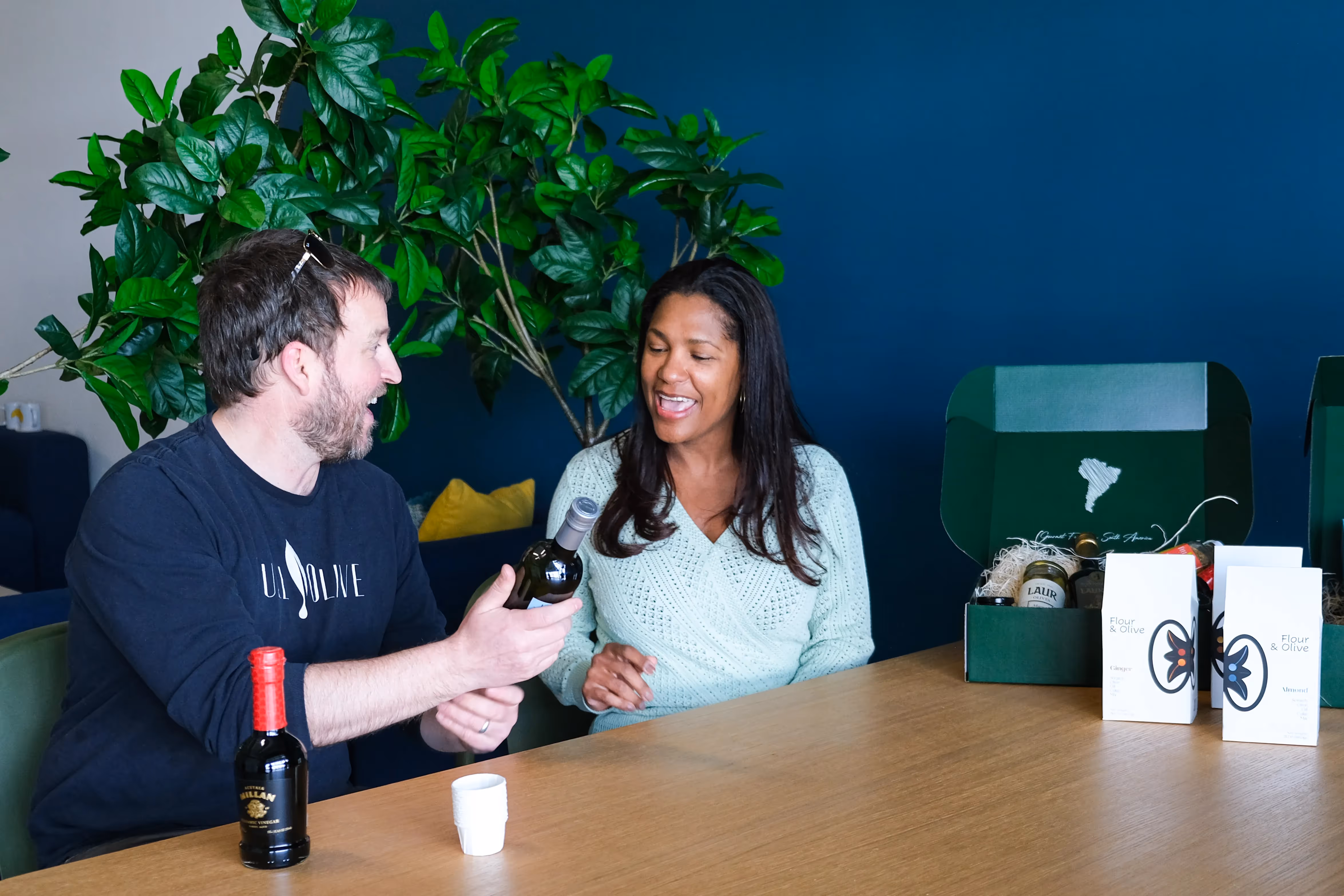 Two small business owners sitting at a table looking at their products and conversing.