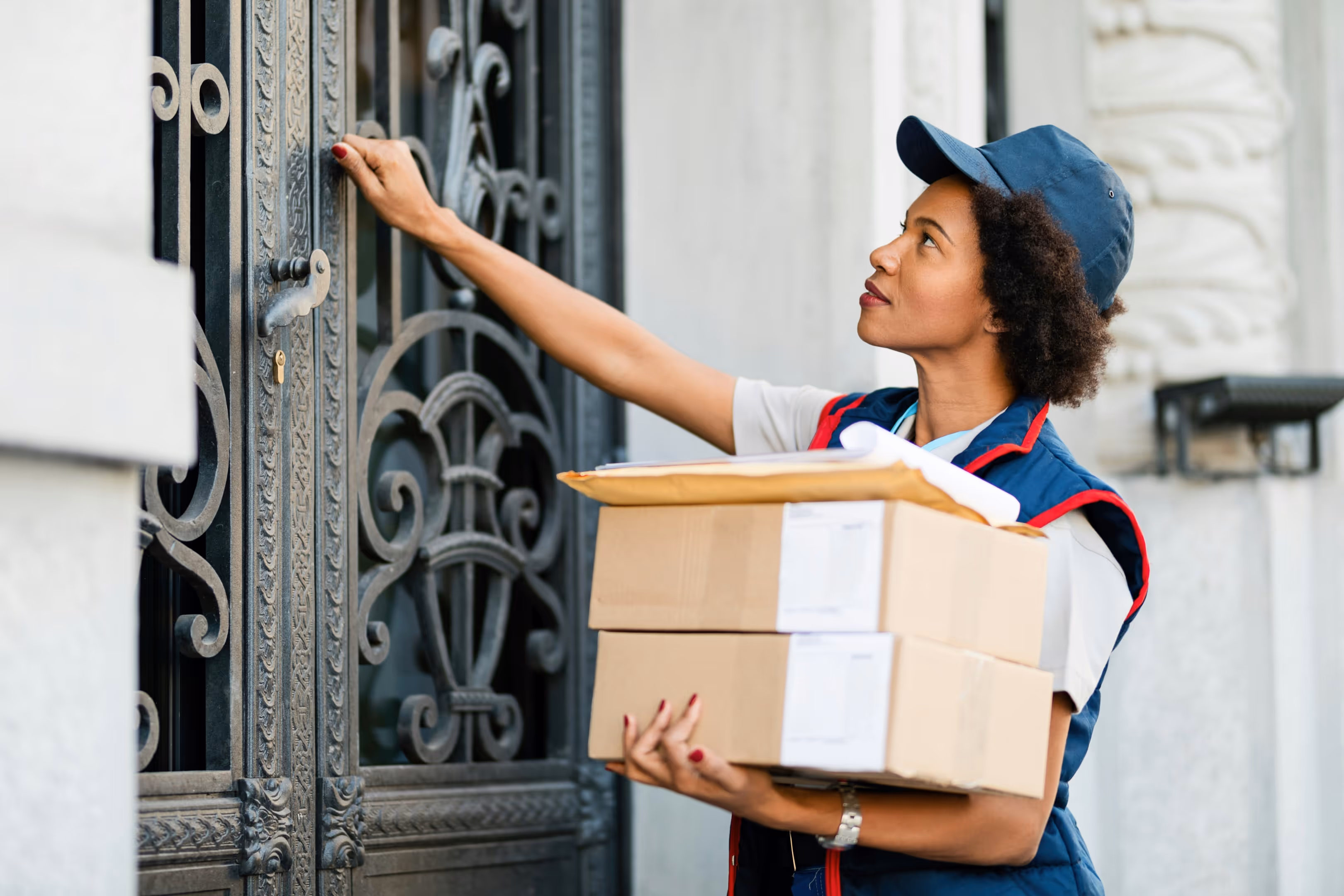 A delivery person knocking on a residential door while holding multiple packages