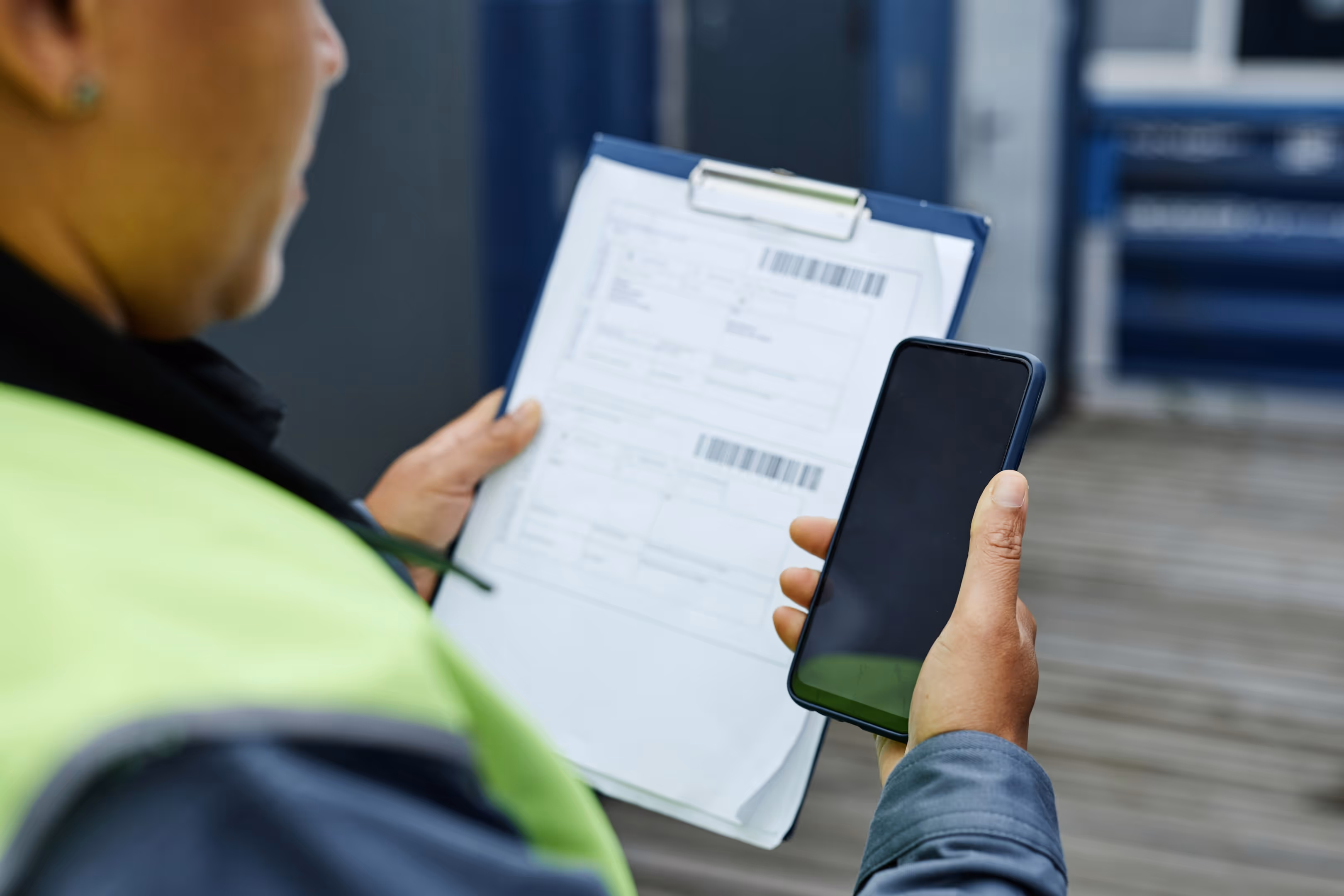 A person holding a clipboard with shipping labels while looking at an iPhone with information on the screen