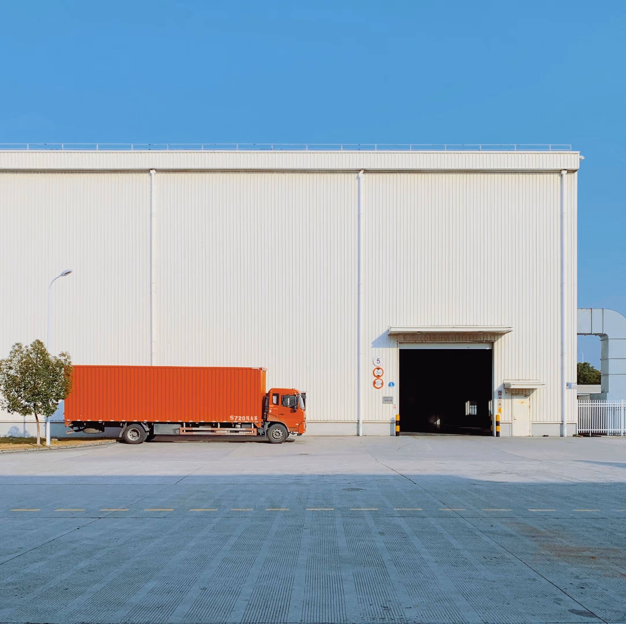 A red freight truck in front of a white warehouse with an open door