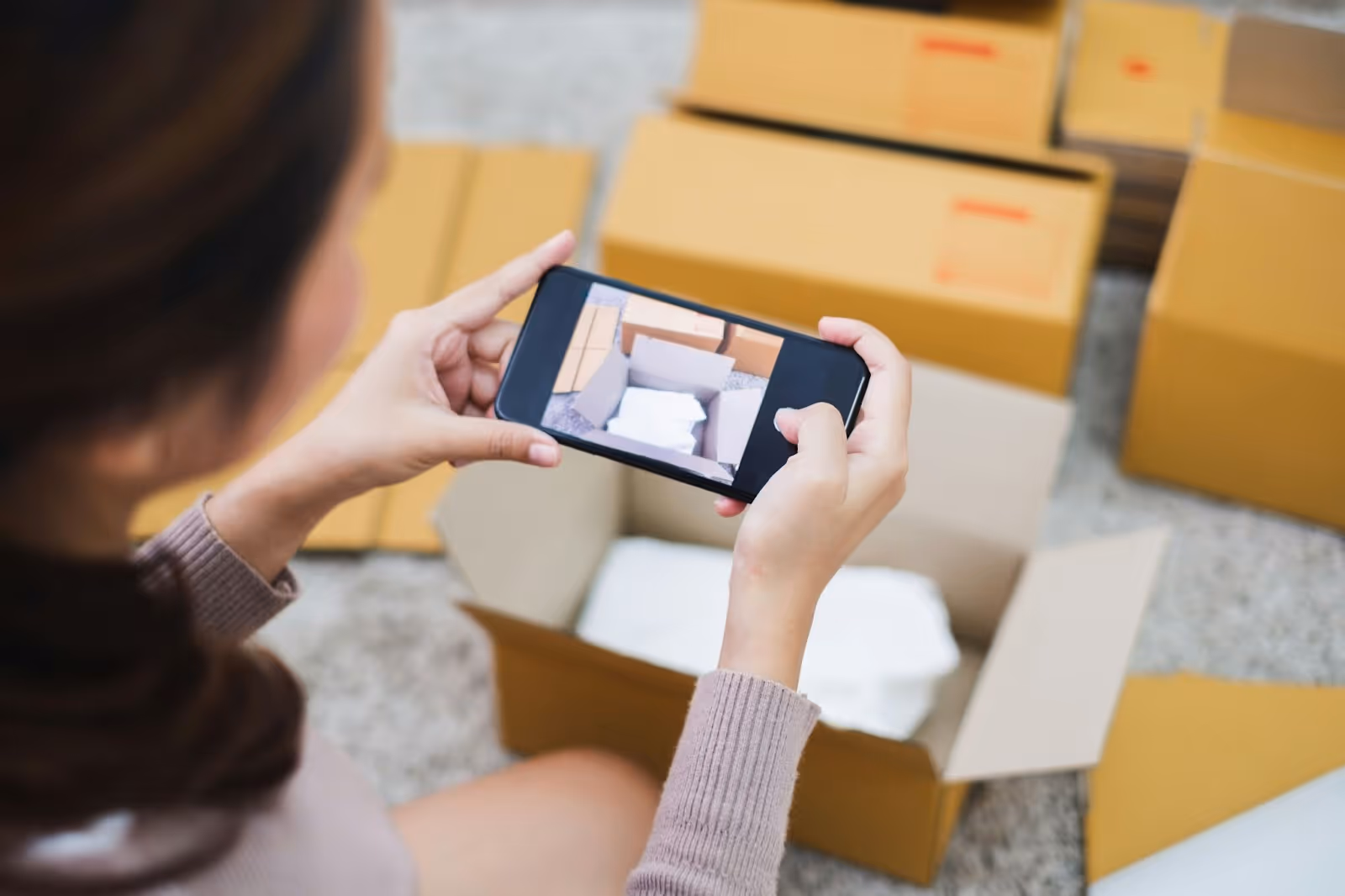 A woman taking photos of a product in a box on her iPhone.