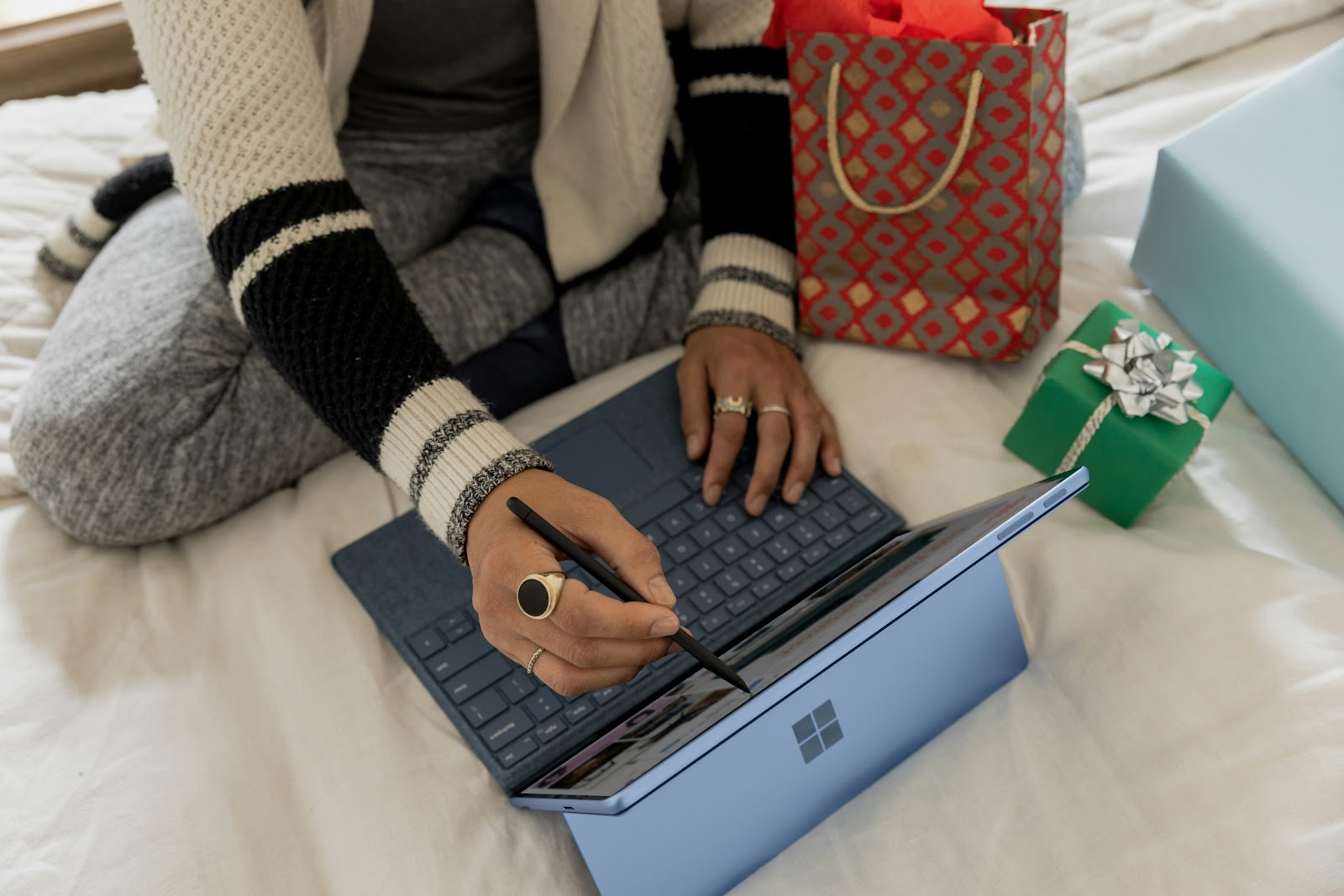 A persona sitting on their bed working from a tablet, with holiday gifts sitting next to them