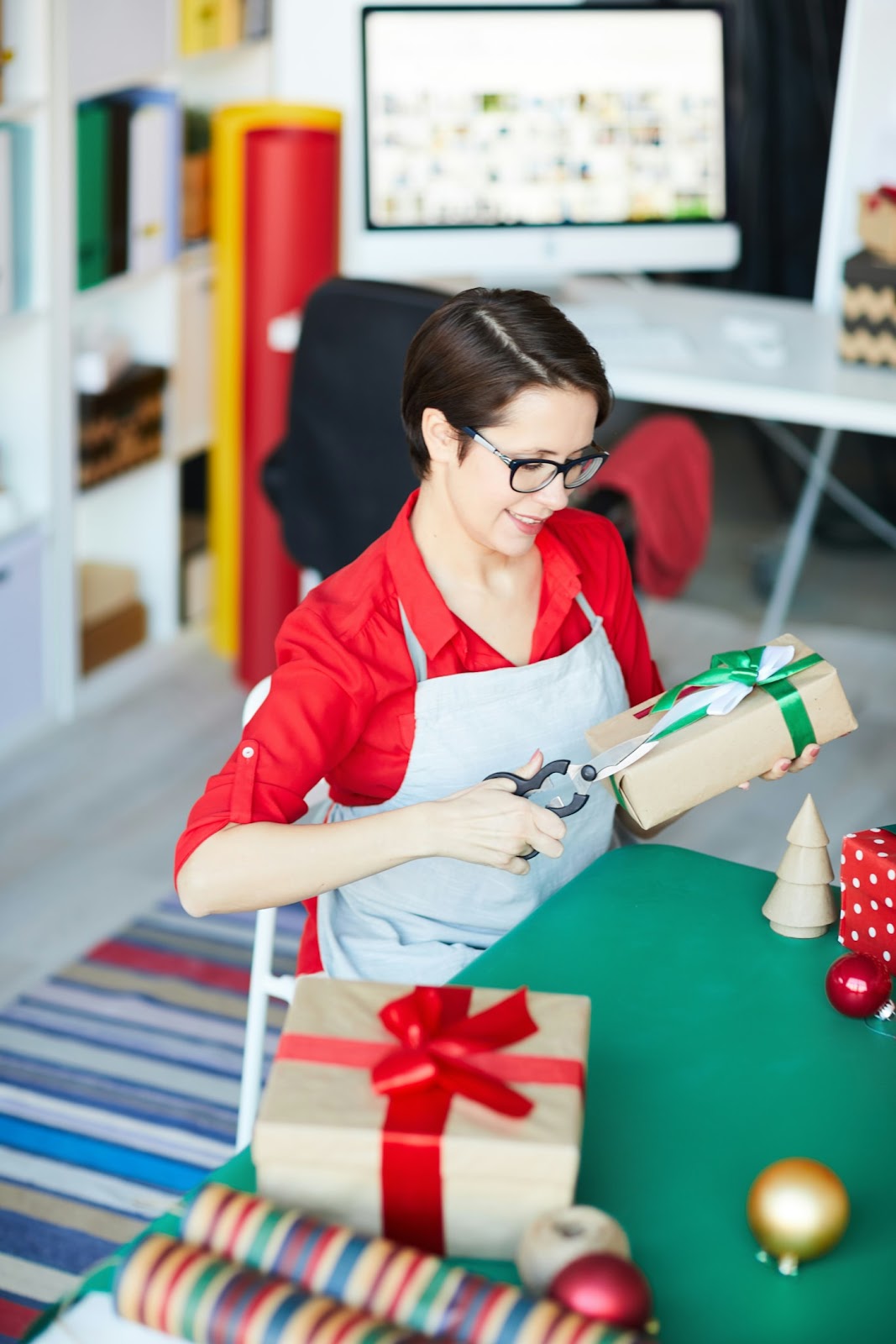A person in an apron sitting at a table wrapping gifts for the holidays
