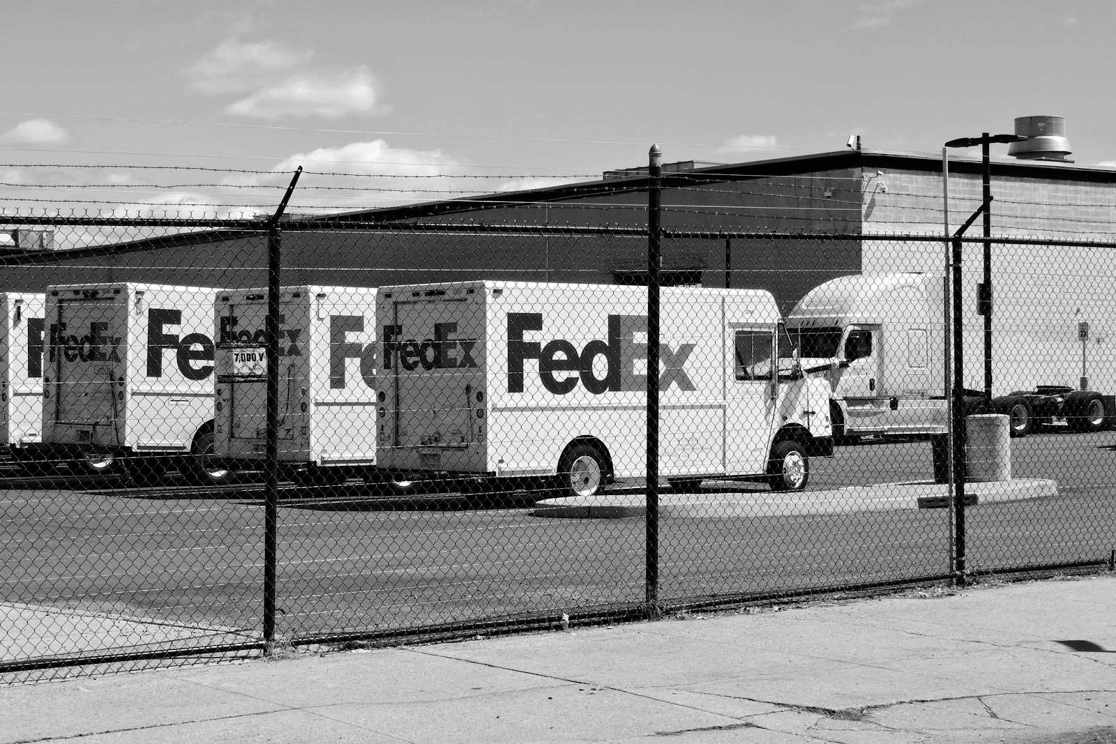 Several FedEx shipping trucks behind barb wire fencing.