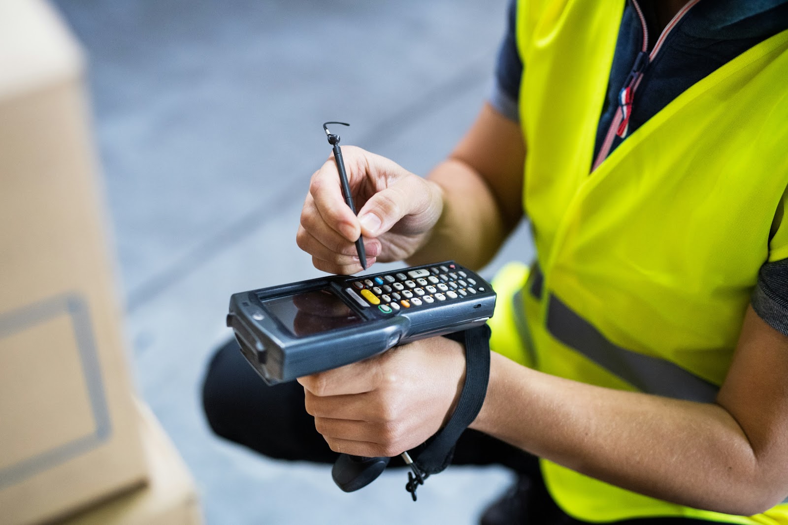 A warehouse worker in a bright-colored safety vest using a scanner to scan inventory boxes.