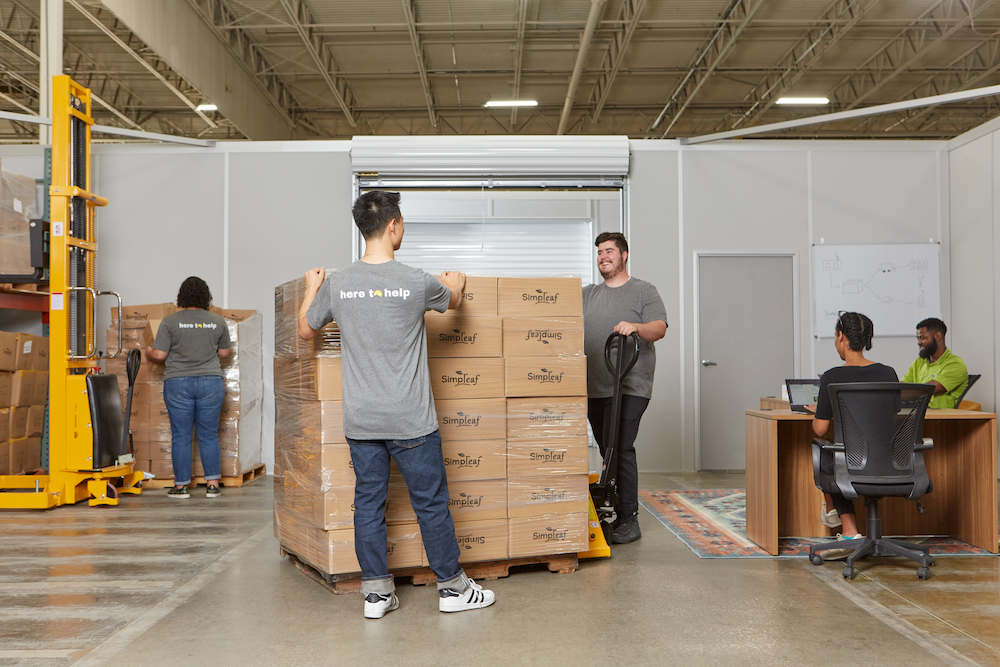 Two men receiving freight at a warehouse while others work happily alongside them.