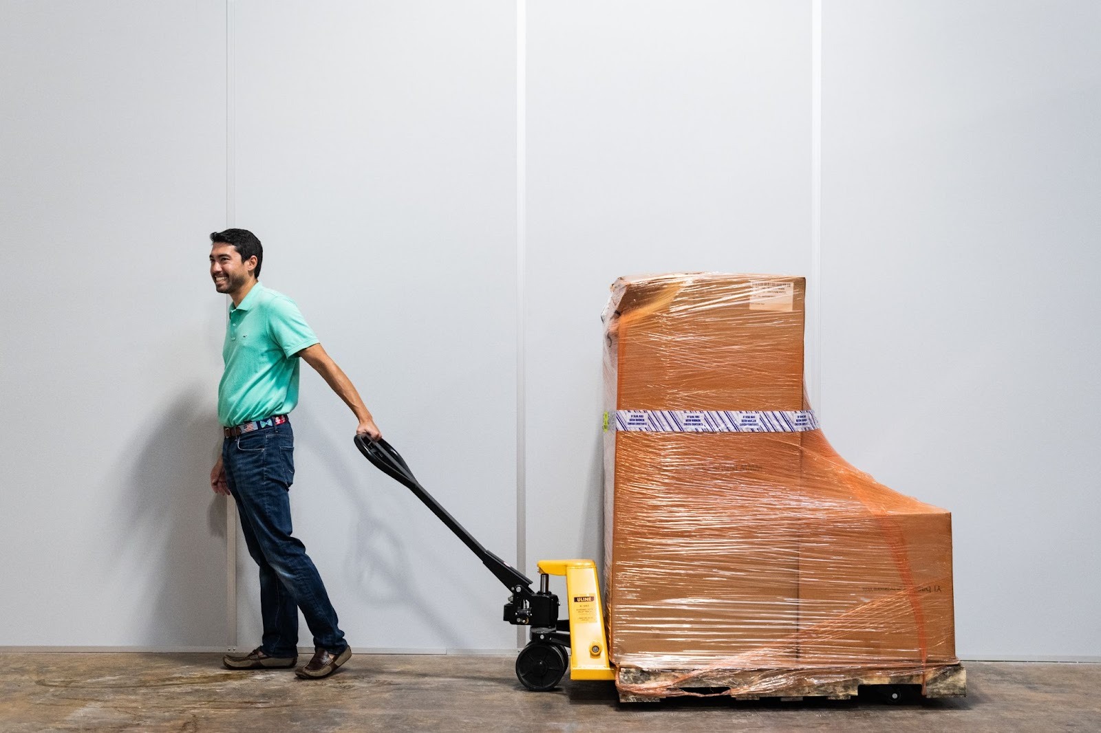 Small business owner pulls inventory on a pallet jack through an ecommerce warehouse.