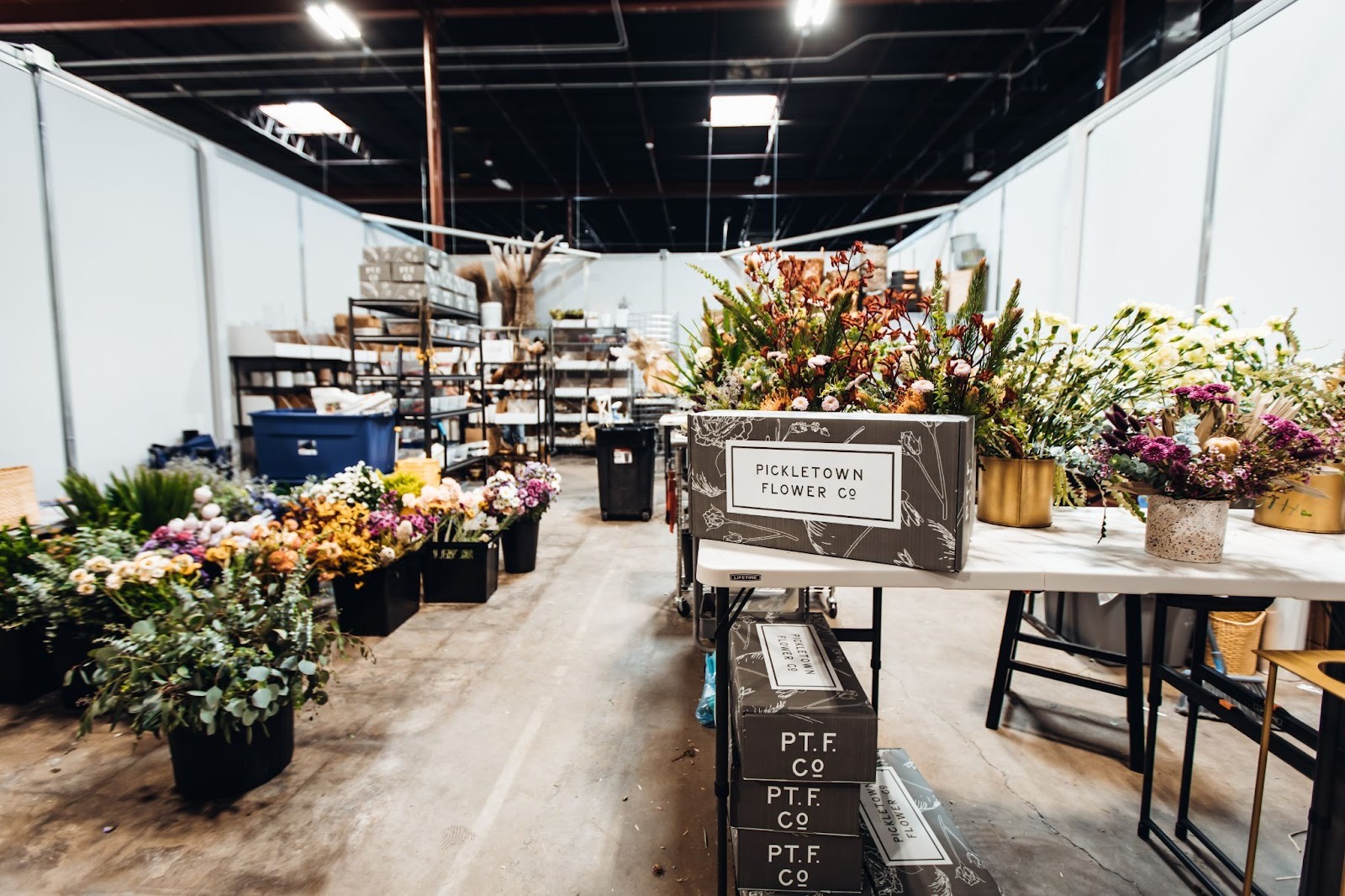 Rows of flowers line the floor of a small bay warehouse space where a floral company prepares orders.