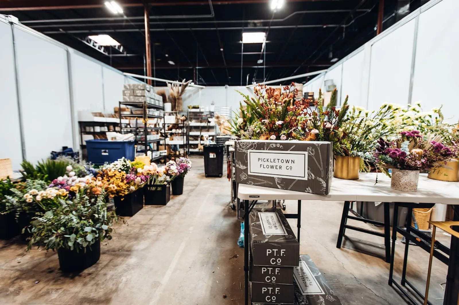 Rows of flowers line the floor of a small bay warehouse space where a floral company prepares orders.