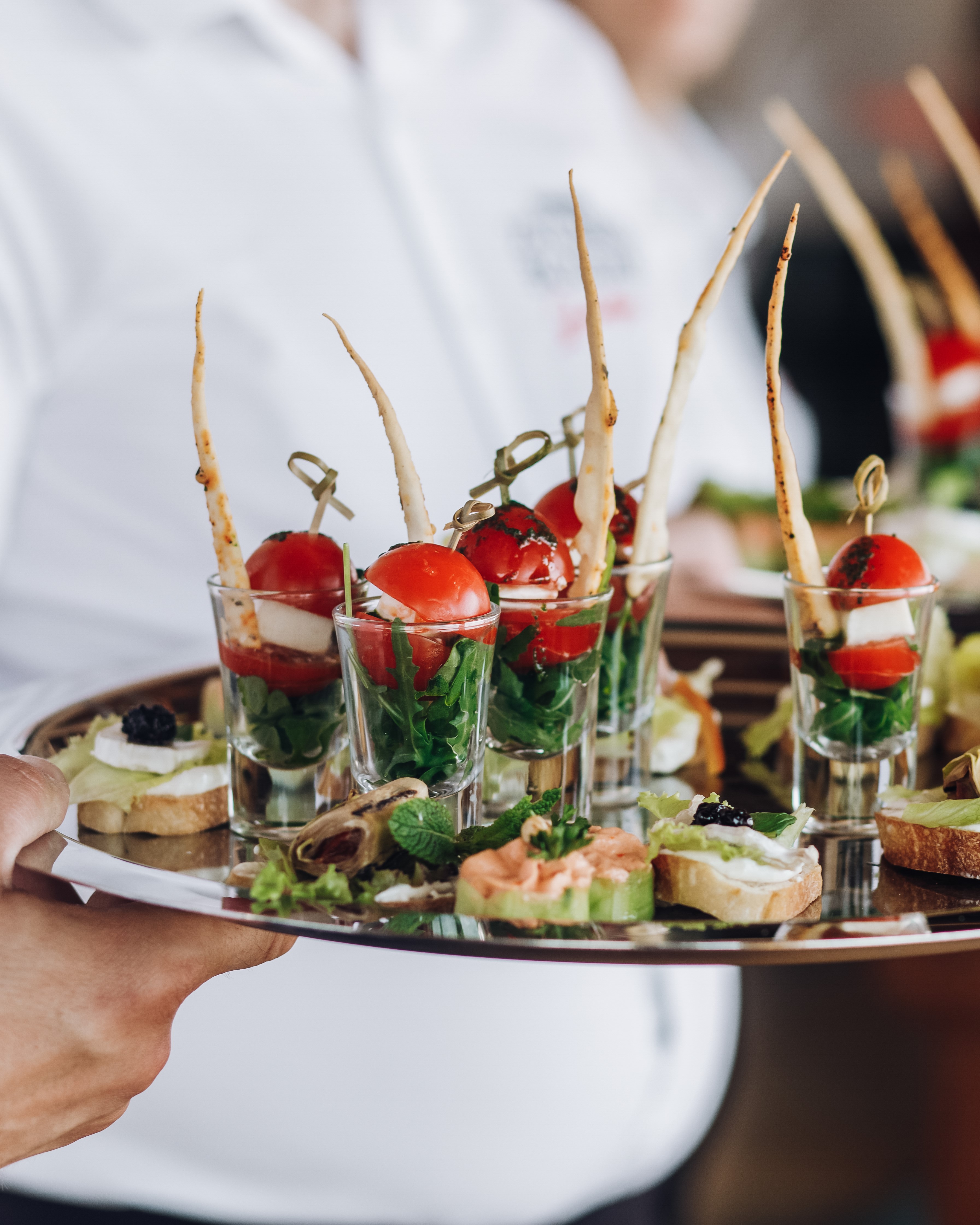 Server holding a tray of canapes and individual tomato appetizers.