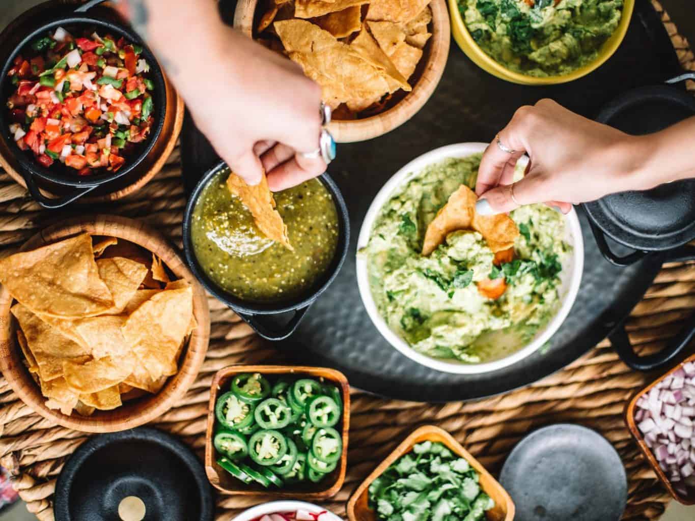 Tortilla chips, guacamole, salsa, and sliced jalapenos arranged for sharing.