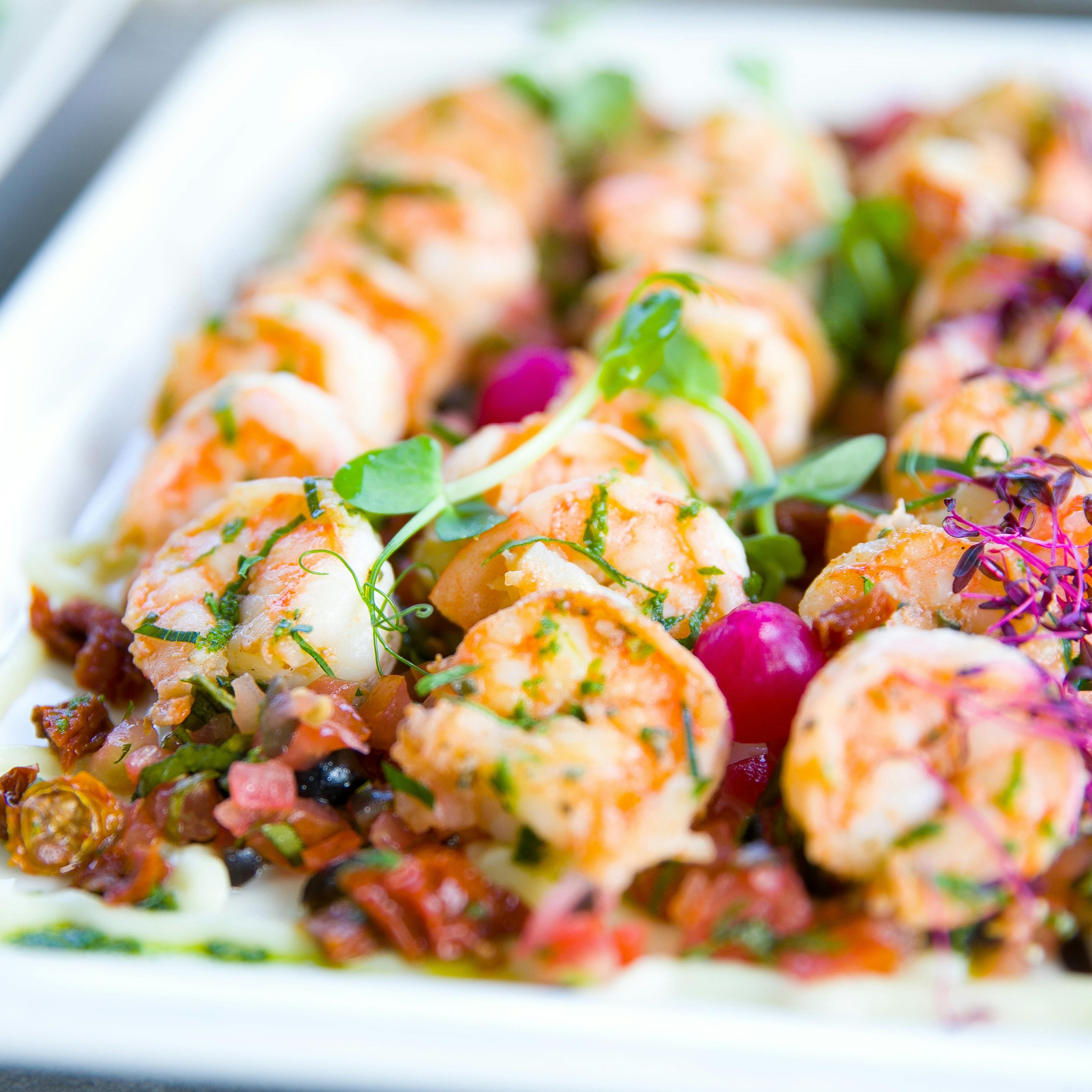 A platter of shrimp appetizers with colorful vegetables and herb garnish.