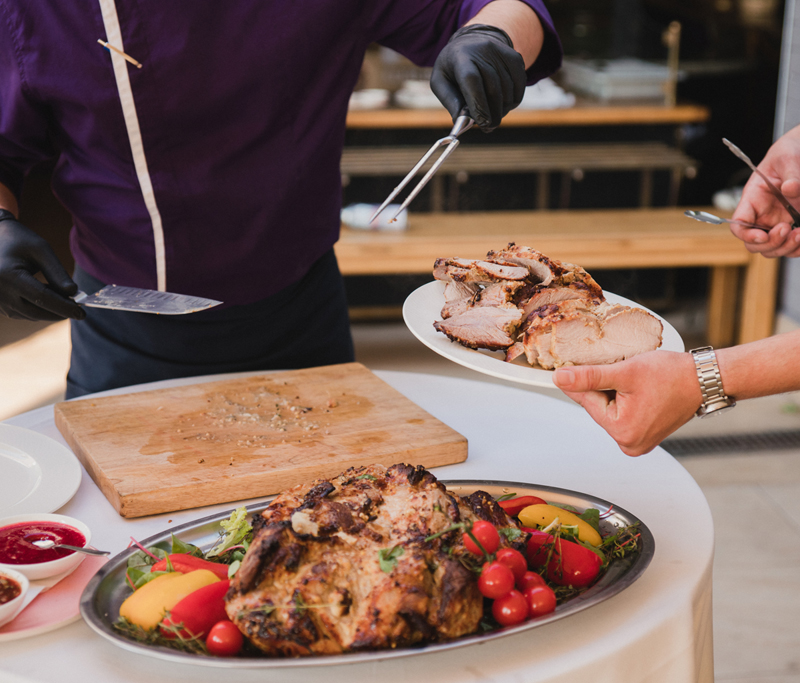 A cook serving sliced roast meat from a carving station.