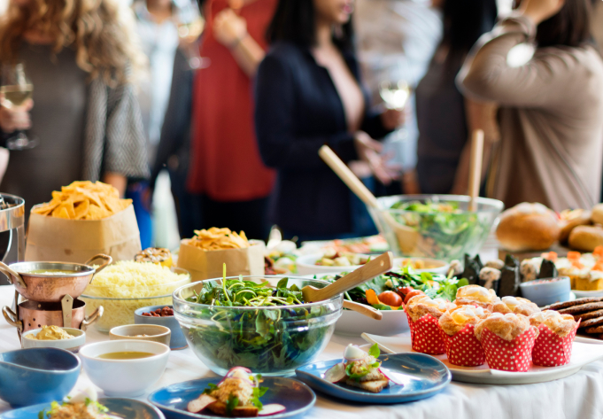 A buffet table with salads, sandwiches, fruit, and small desserts.