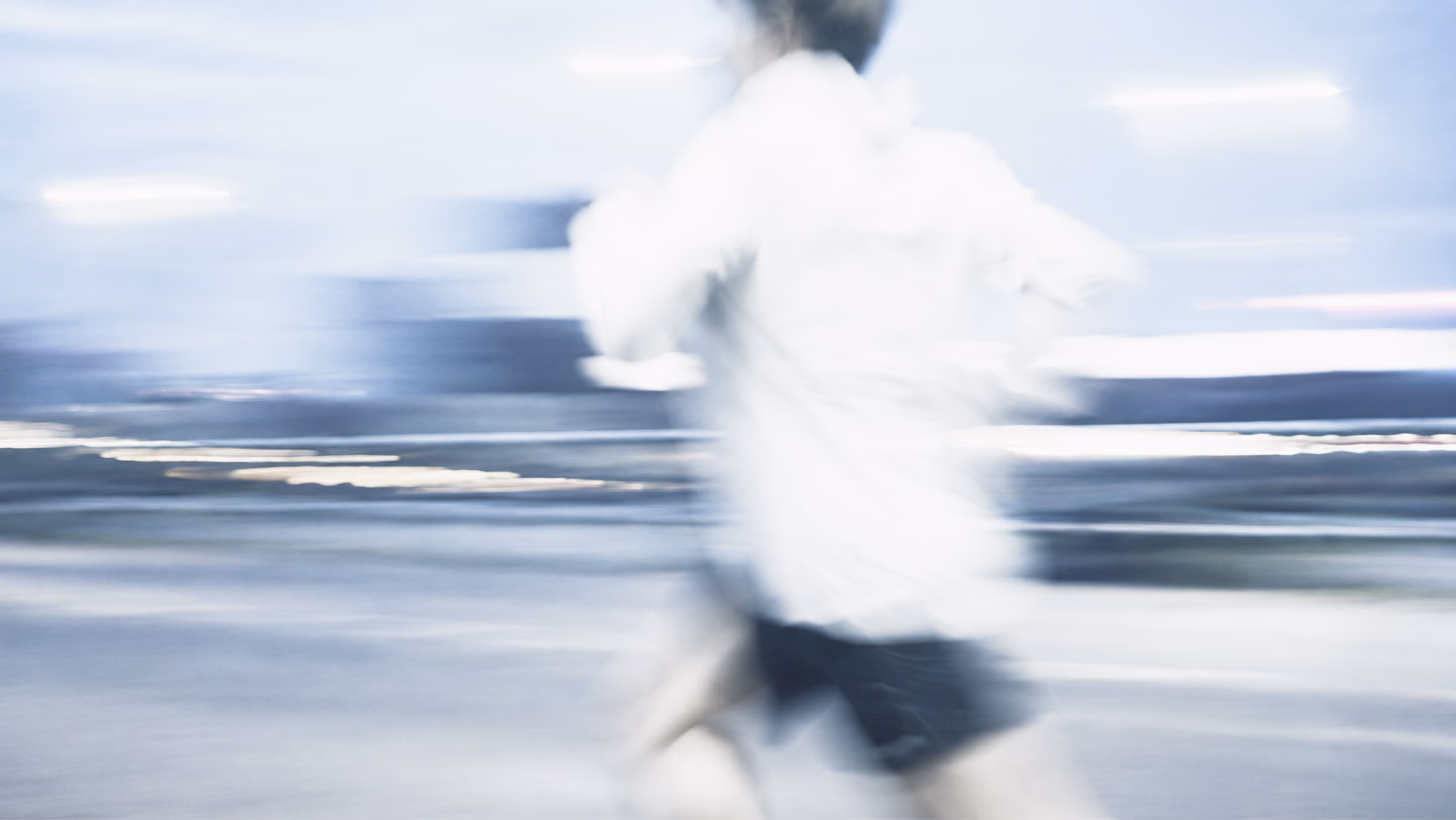 Un homme en tenue de sport court rapidement vers la gauche dans un décor flou bleu-gris.