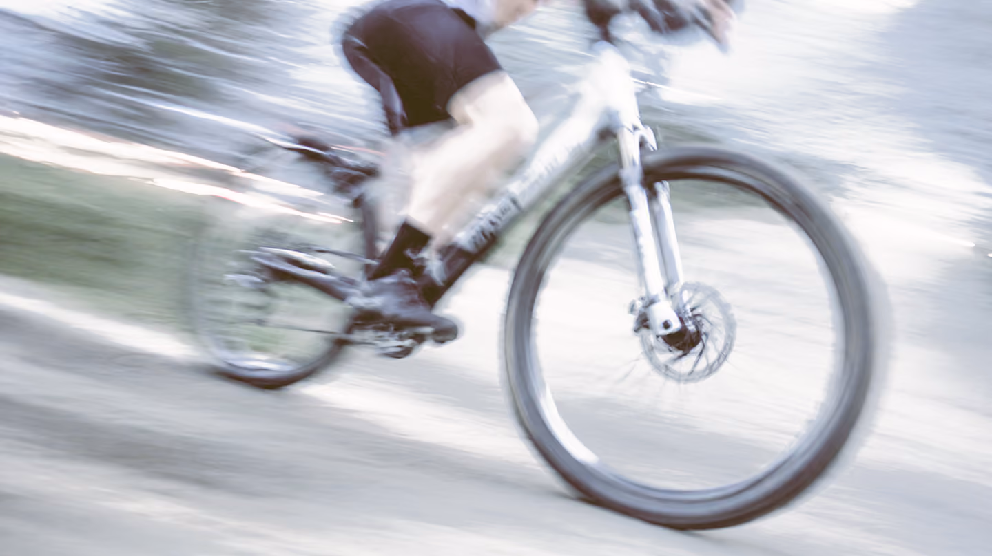 Personne en short noir roulant rapidement à vélo sur un chemin flou.