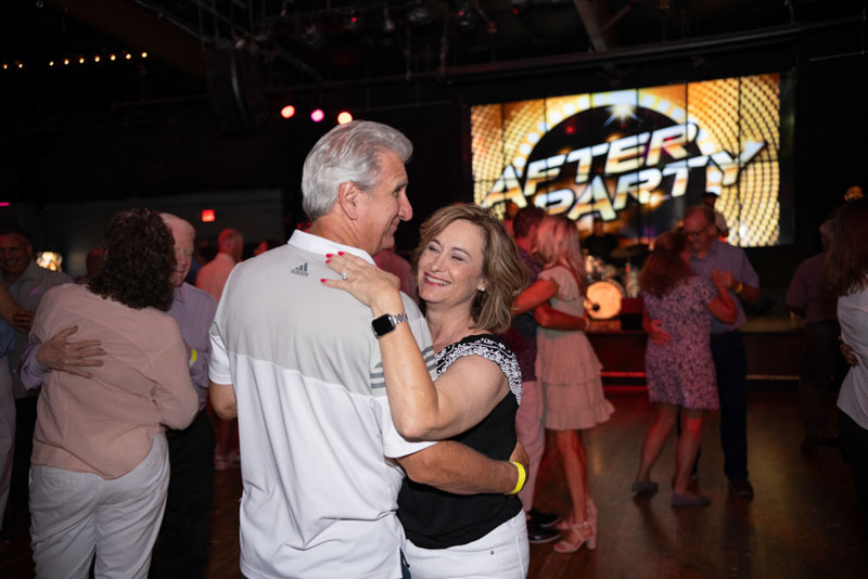Couples dancing closely on a wooden dance floor with a large screen reading 'After Party' in the background.