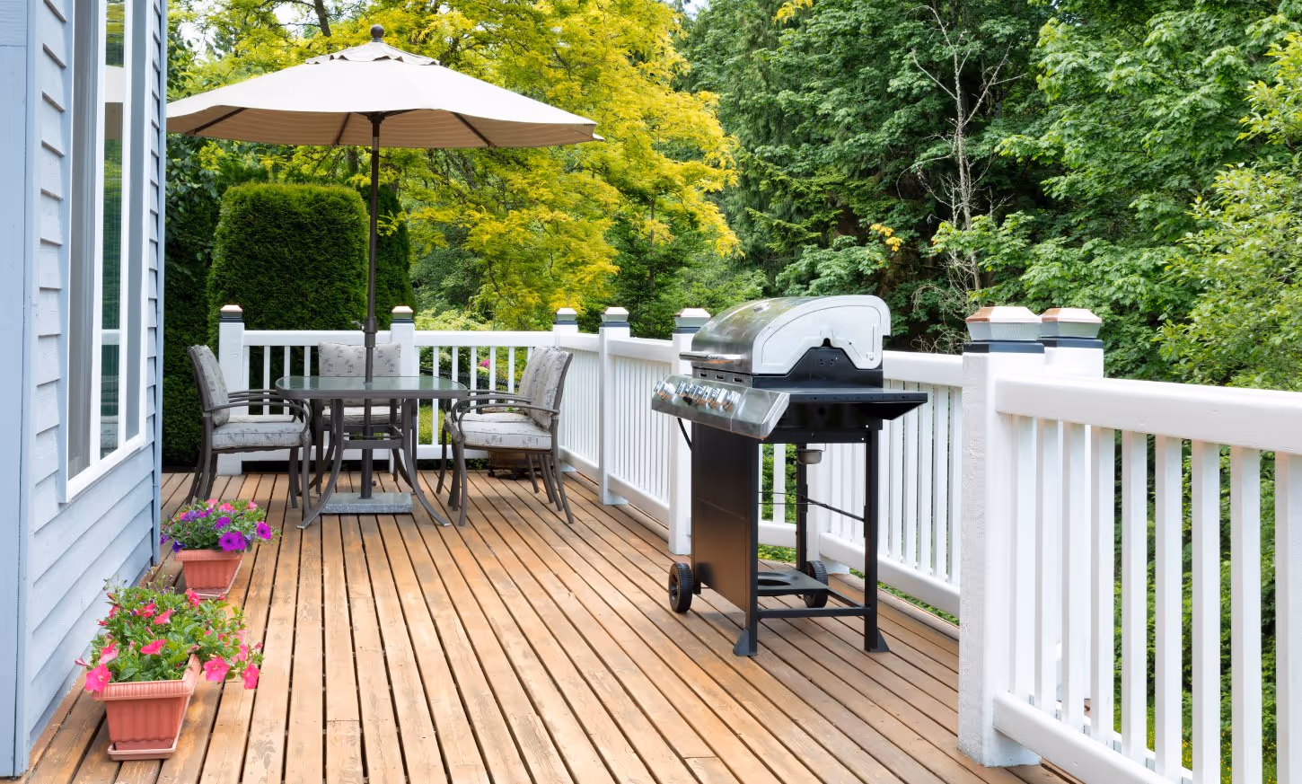 Wooden deck with grill, table, chairs, and umbrella.