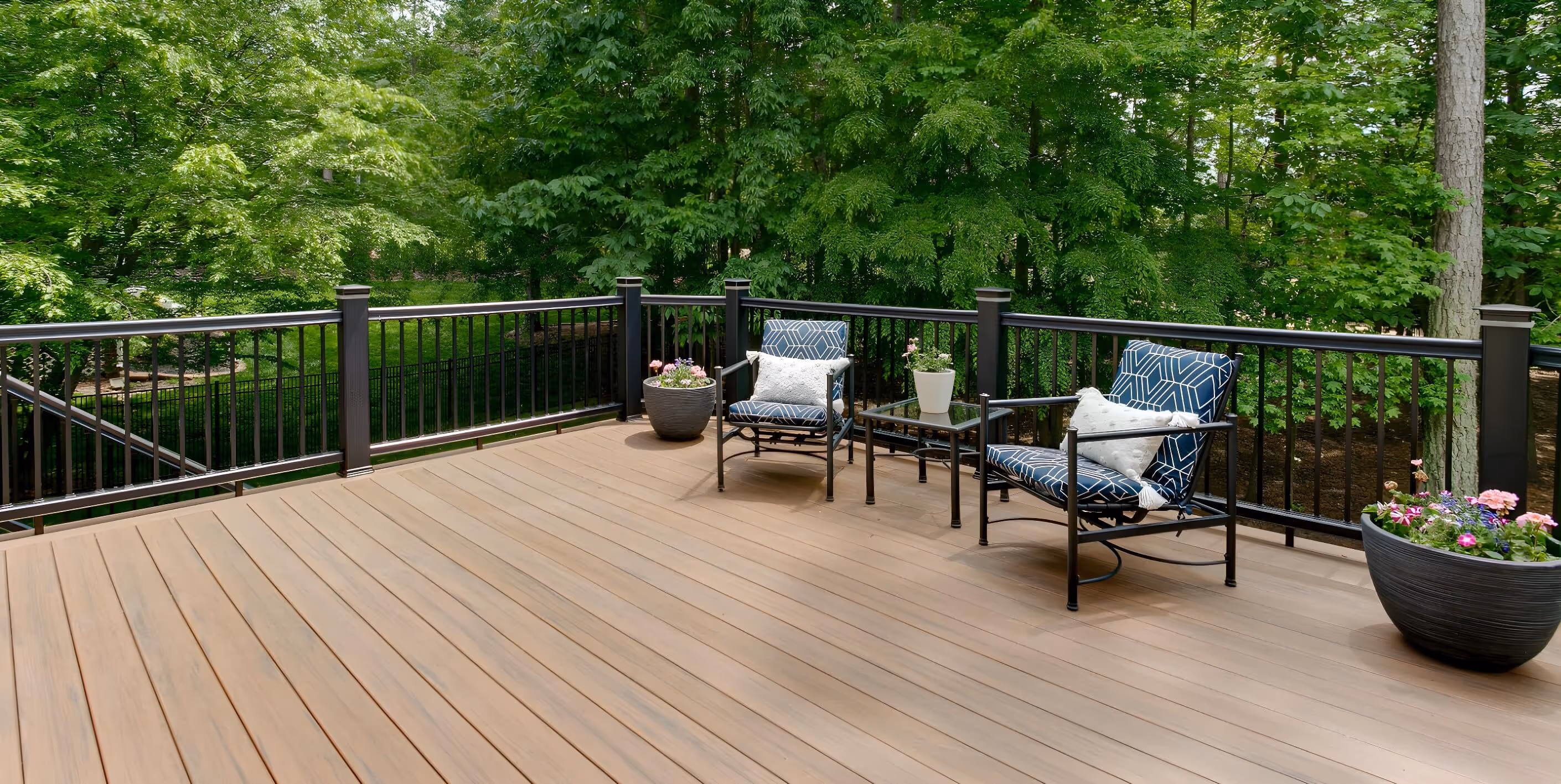 Spacious wood deck with two chairs, small table, surrounded by trees.