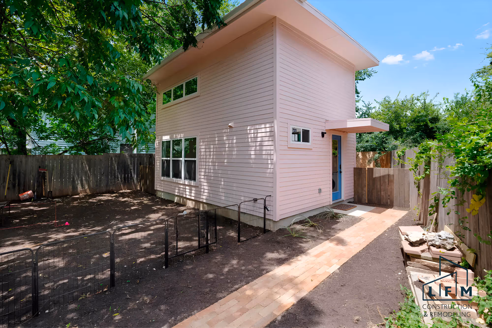 Modern backyard with pink house, trees, and LFM Construction logo.