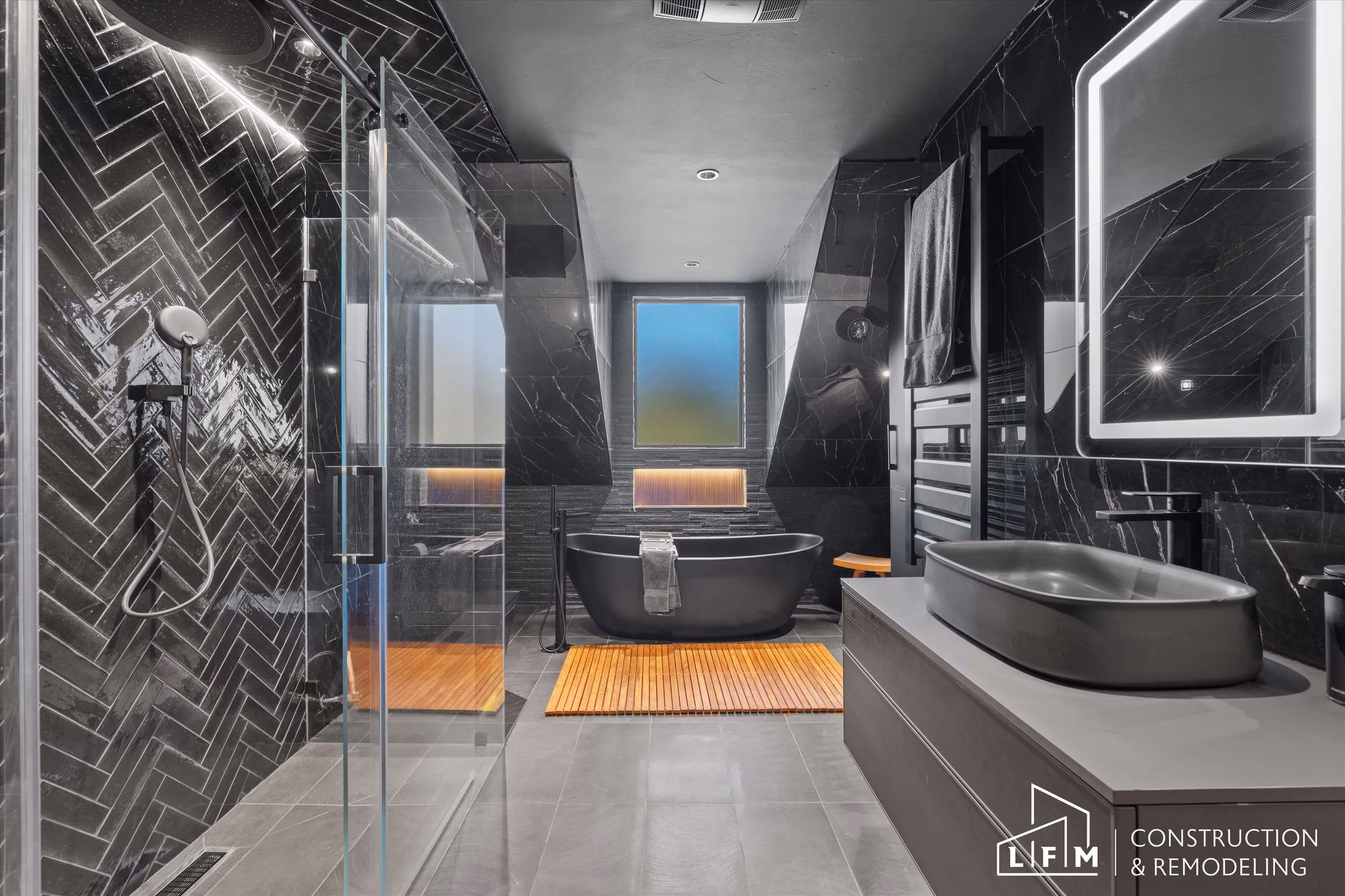 Modern luxury bathroom with black herringbone tiles, freestanding tub, and LFM Construction & Remodeling logo.
