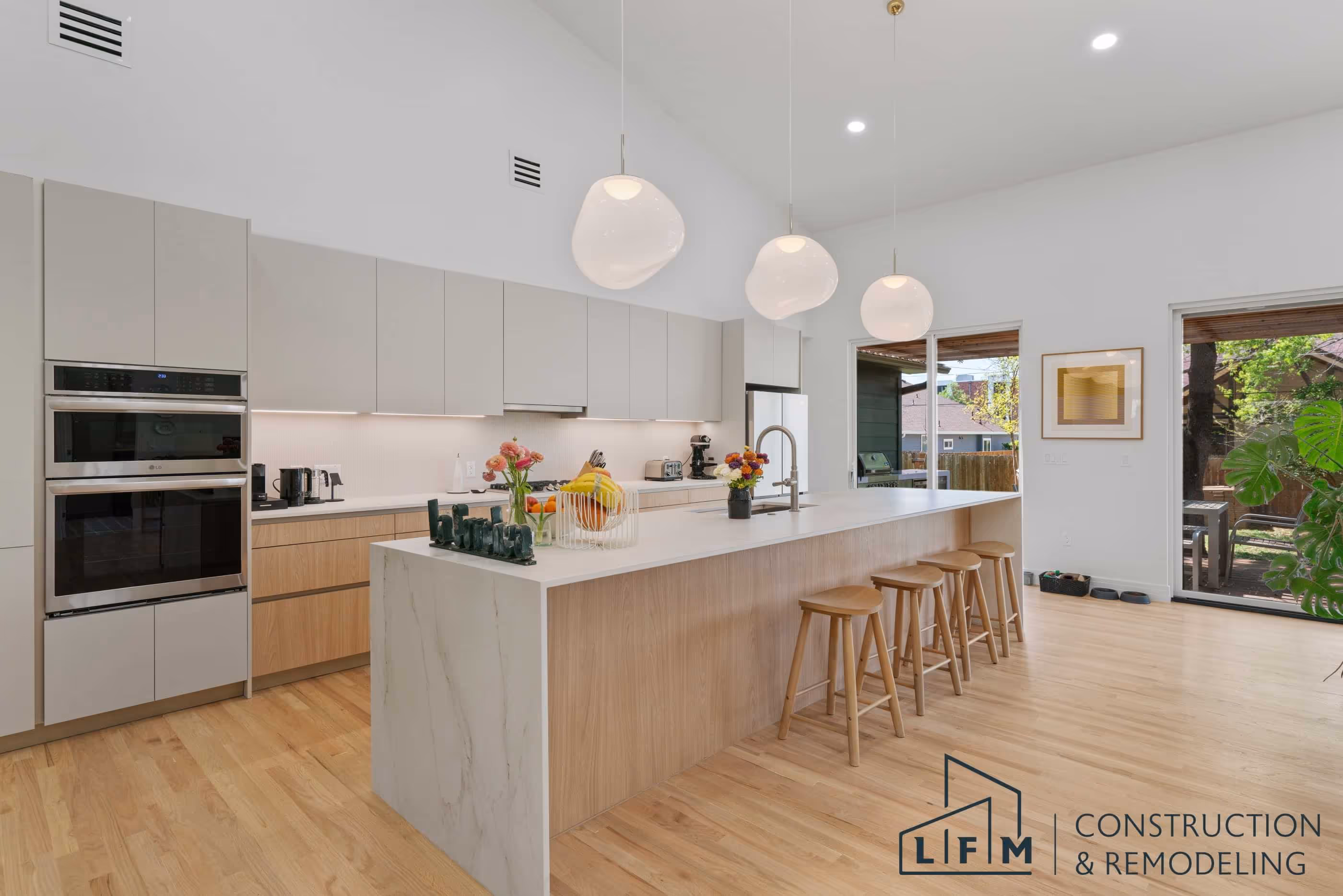 Modern kitchen with island, barstools, pendant lights, and LFM Construction logo.