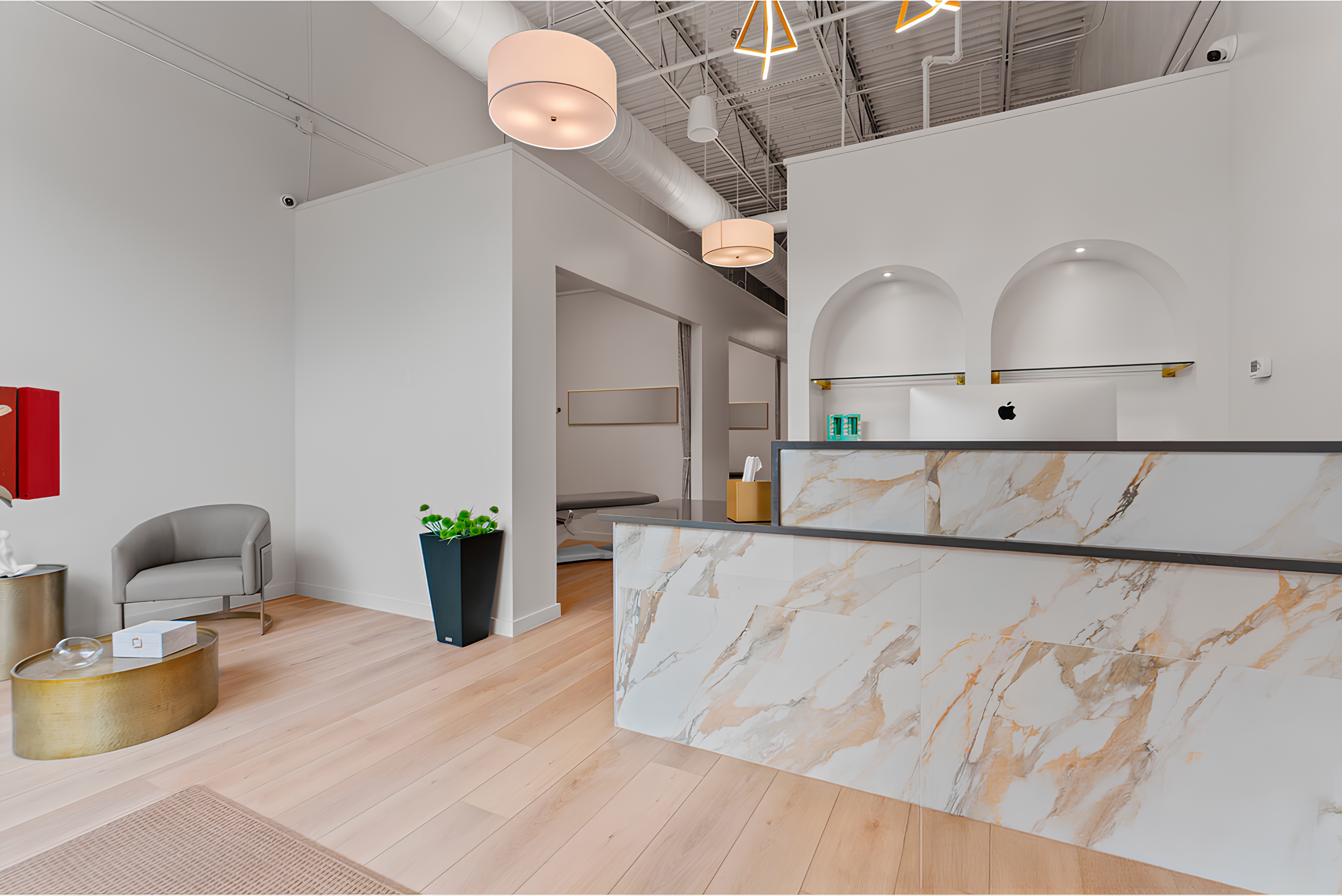 Modern reception area with marble desk, gray armchair, and decorative lighting in a minimalist office setting.
