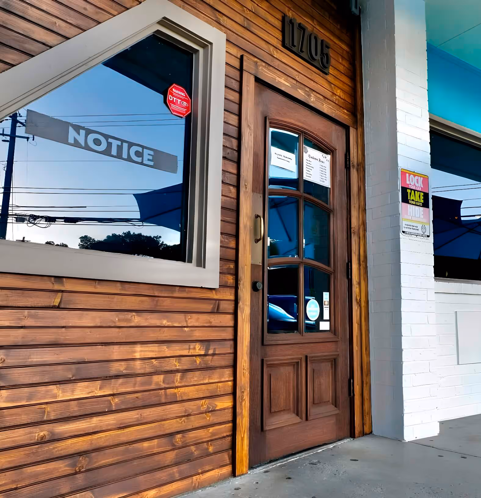 Wooden door and window of a modern storefront with blue umbrellas and security notice signs.