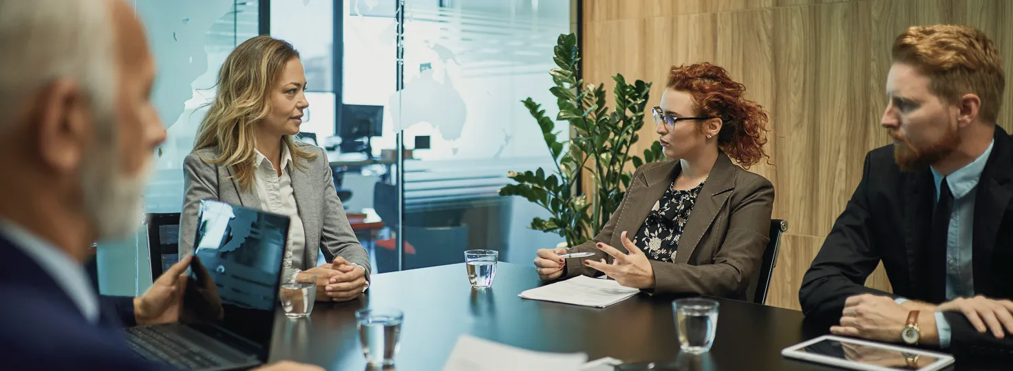 Four professionals engaged in a business discussion around a conference table with laptops, documents, and glasses of water.