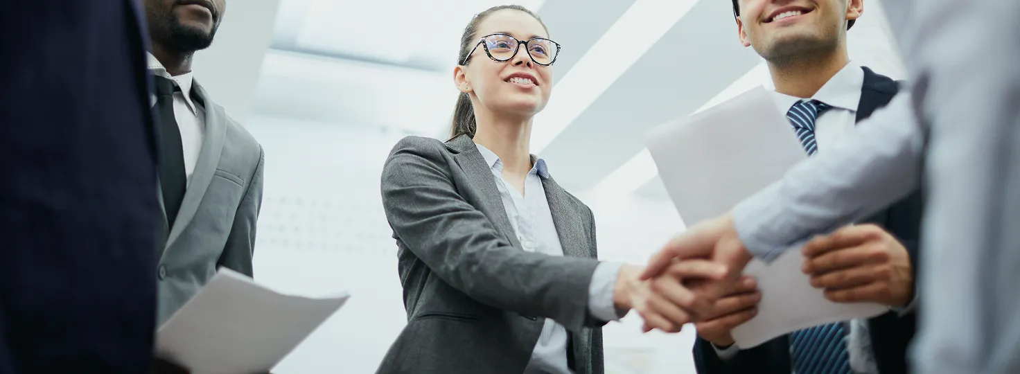 Businesswoman smiling and shaking hands with a colleague during a meeting in a bright office.