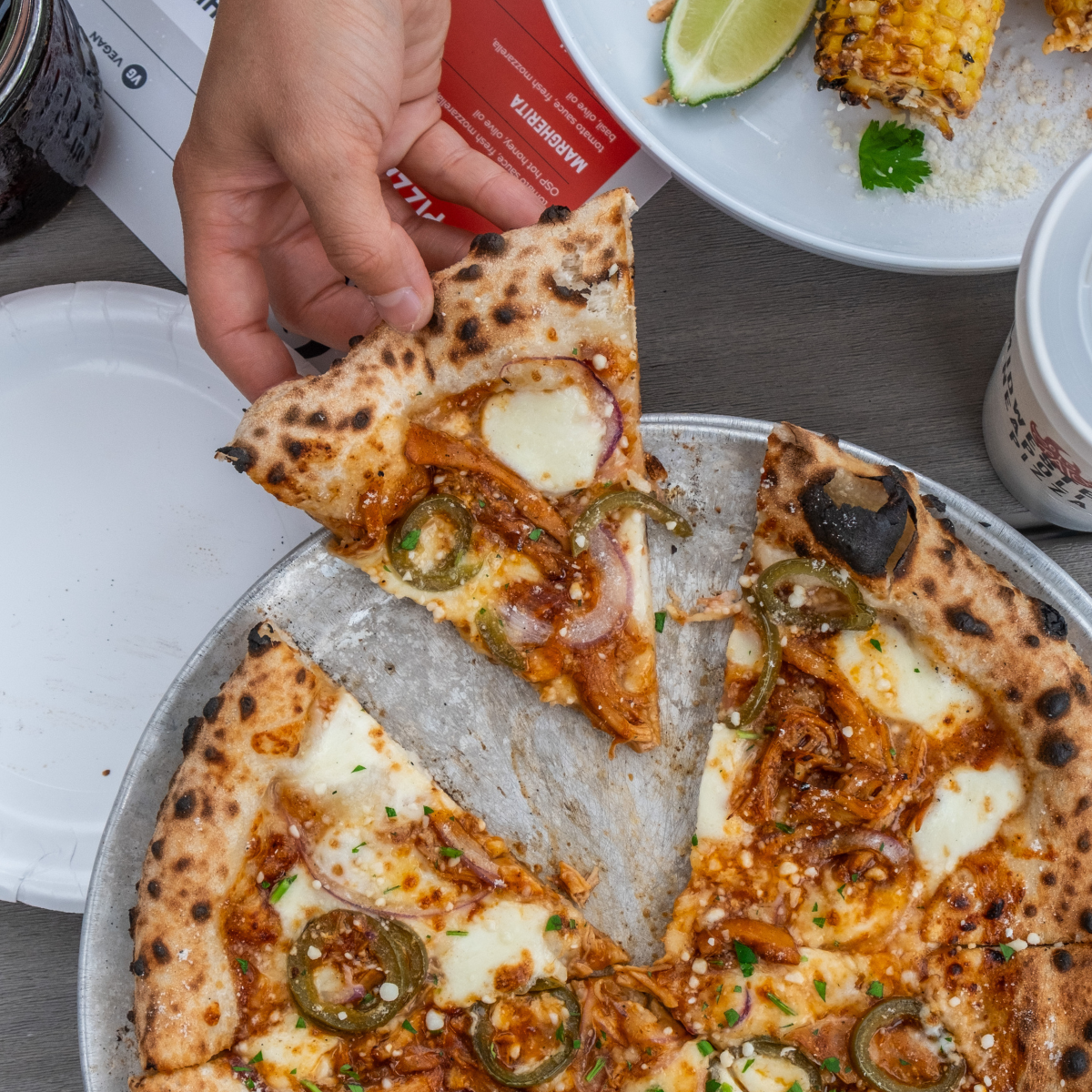 a hand grabbing a slice of pizza off on a tray