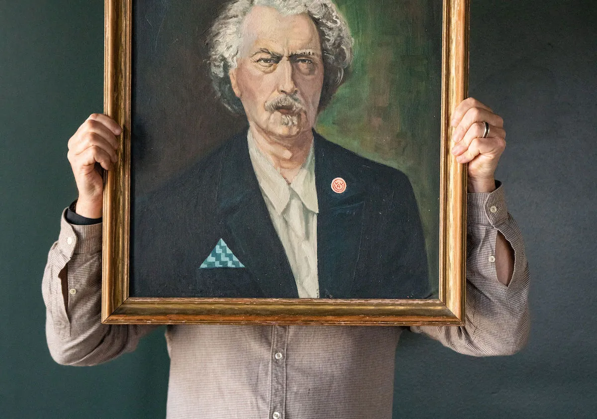 Man holds up oil painting of grumpy patron saint