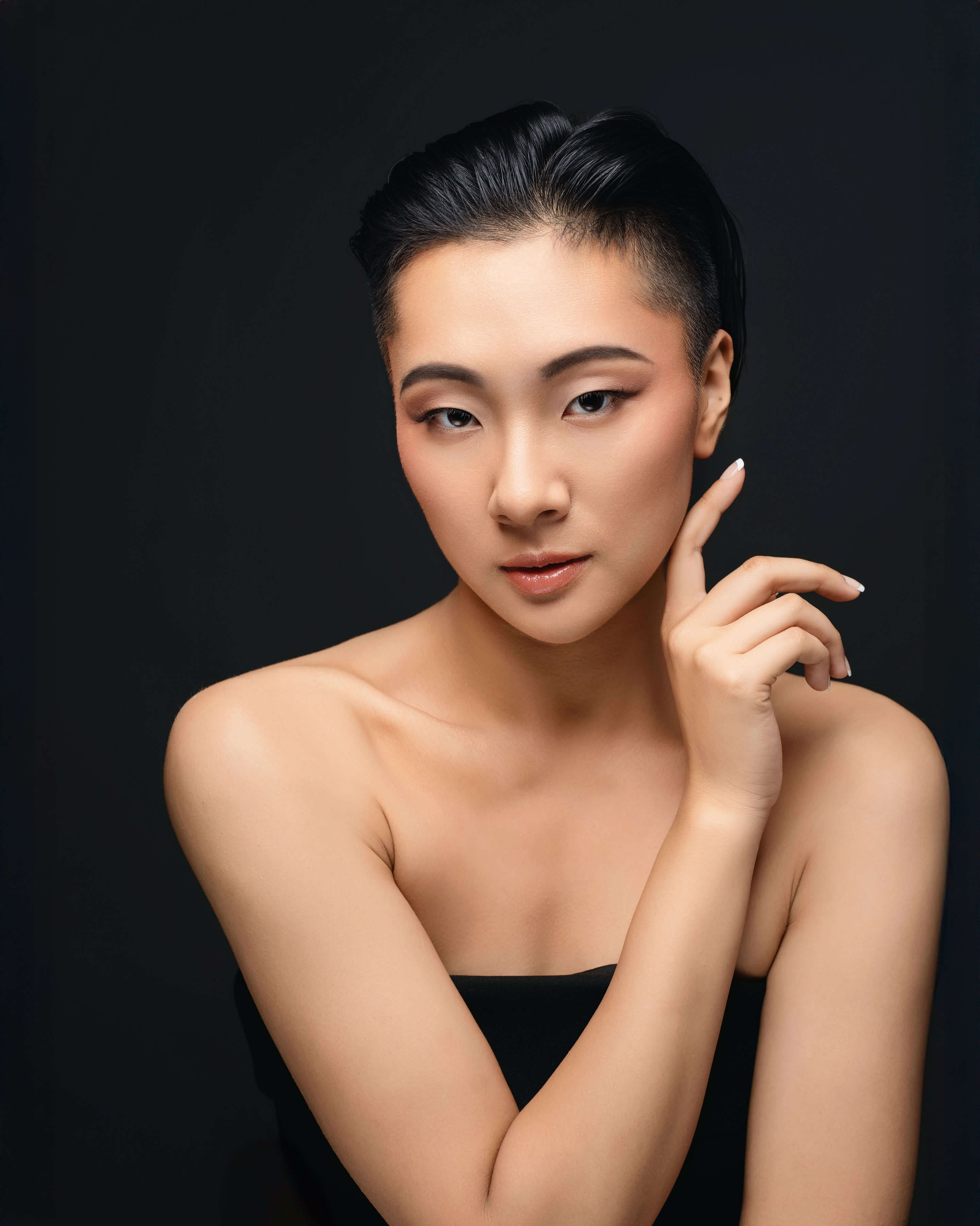 Young Asian woman with flawless makeup, posing hand near face.